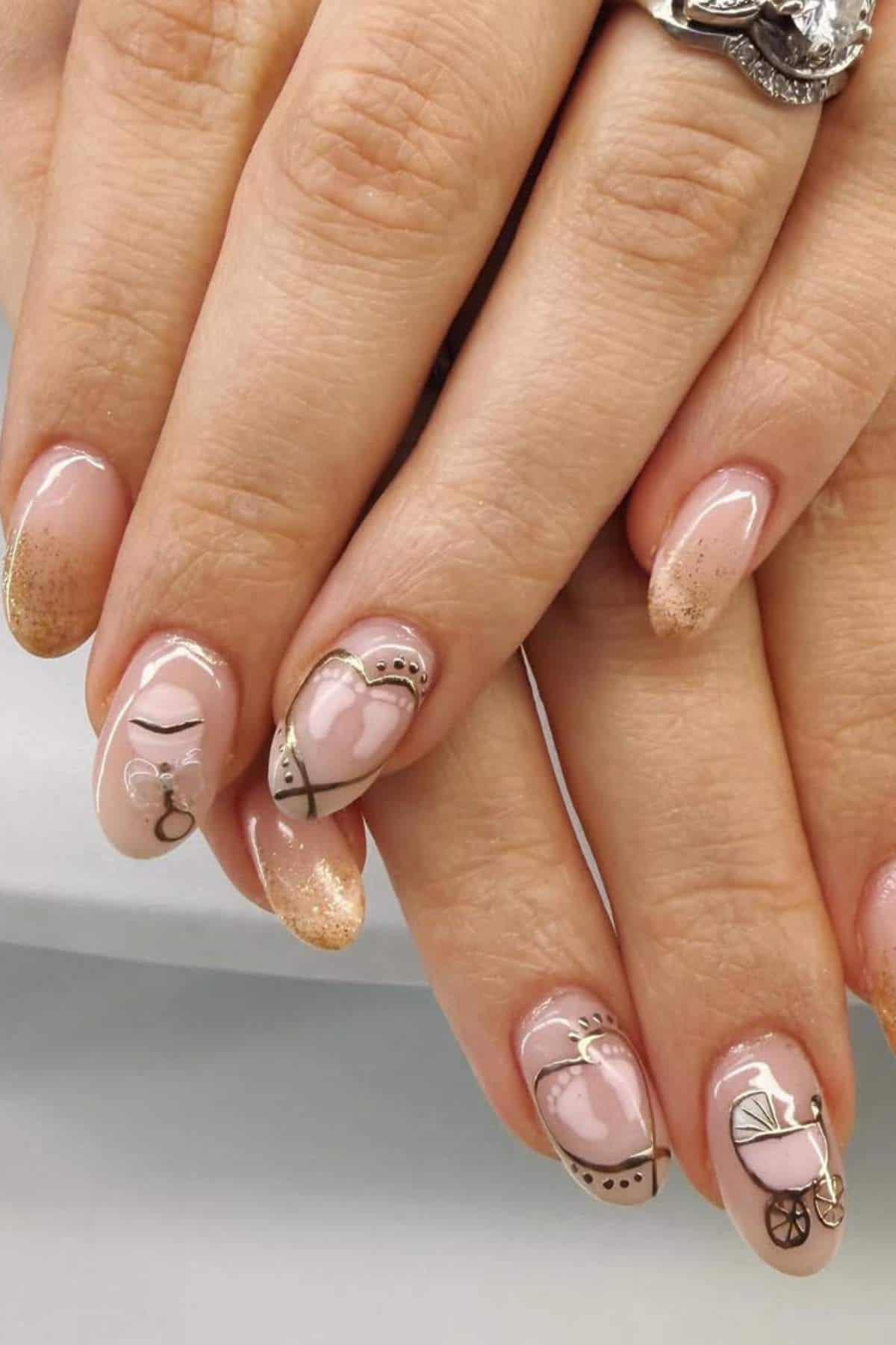 Close-up of hands with manicured nails featuring abstract art designs in nude and gold tones, including hearts, lines, and small decorative elements.