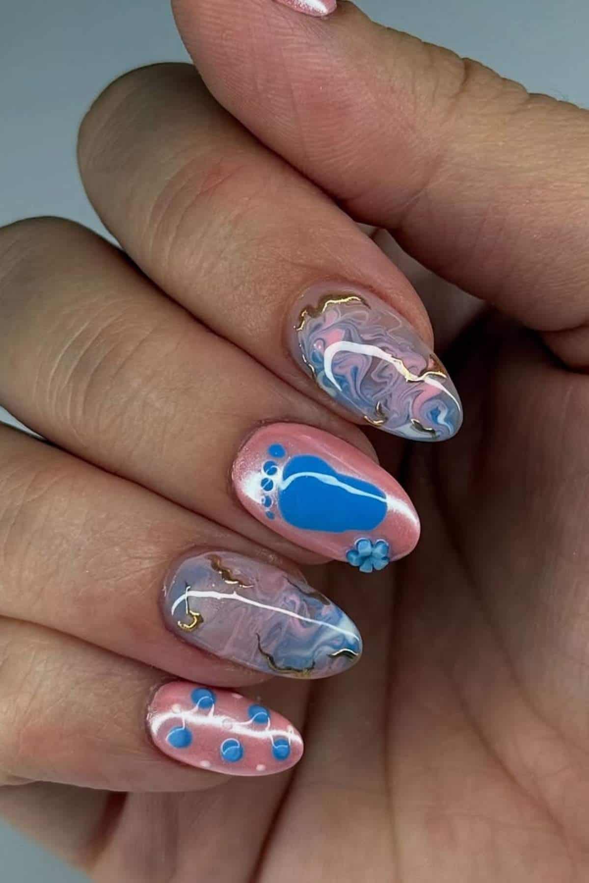 A hand with long nails features pink and blue marbled nail art, including blue footprints, dots, and small 3D flower decorations on two nails.