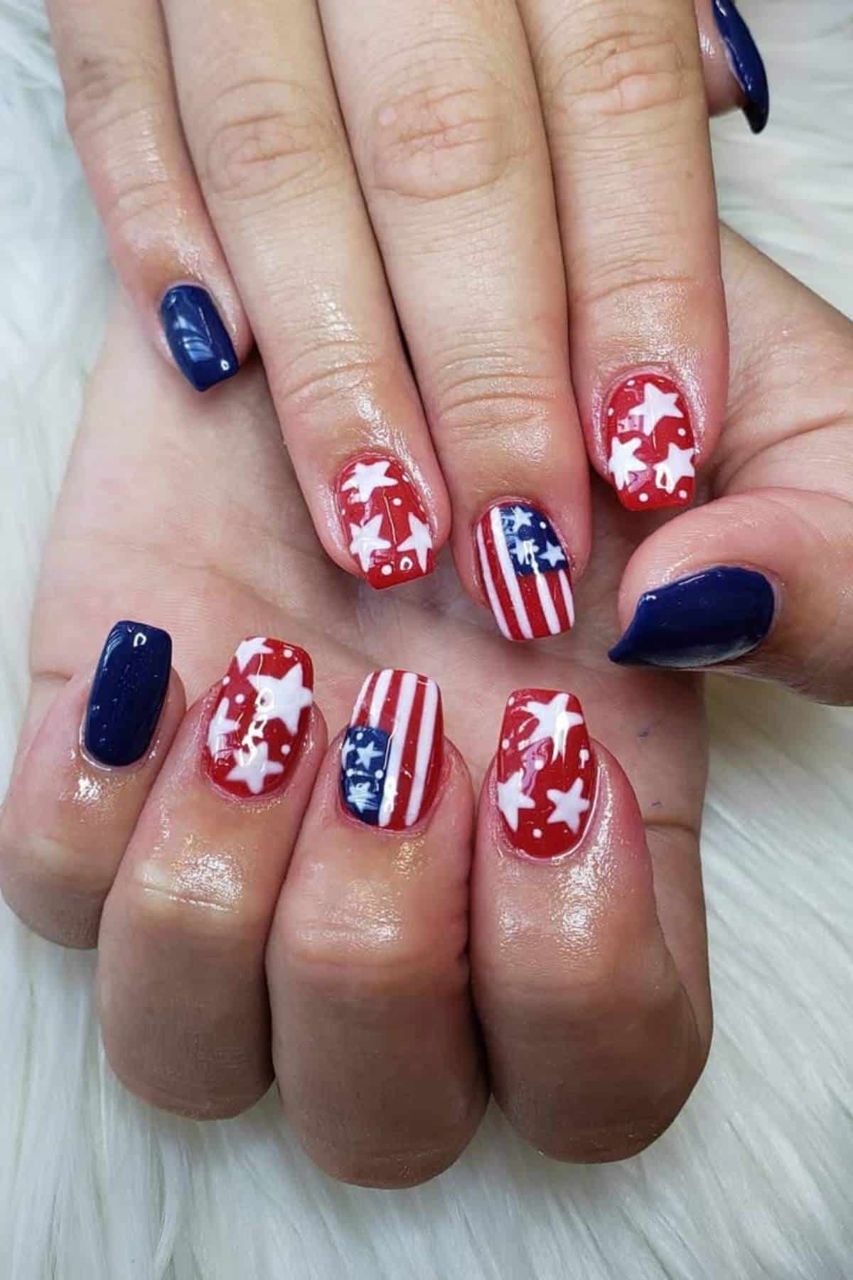 Hands with manicured nails, featuring a patriotic design with blue, red, and white colors, stars, and stripes resembling the American flag.