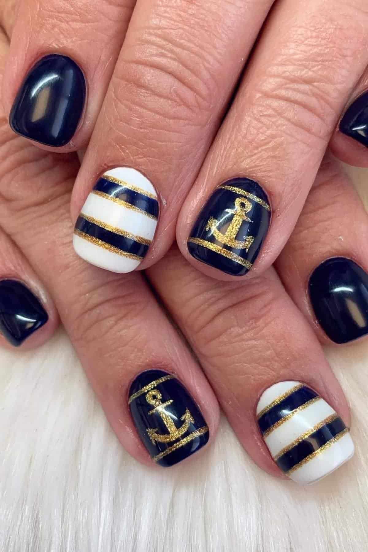 Close-up of hands with navy blue and white striped nails, featuring gold anchors and gold stripe accents on a few fingers.