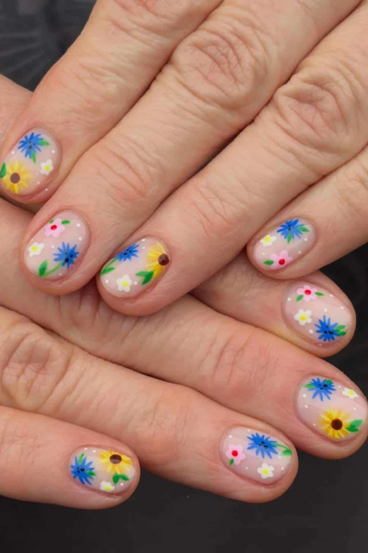 Close-up of hands with short fingernails featuring colorful, hand-painted floral designs on a light pink base.