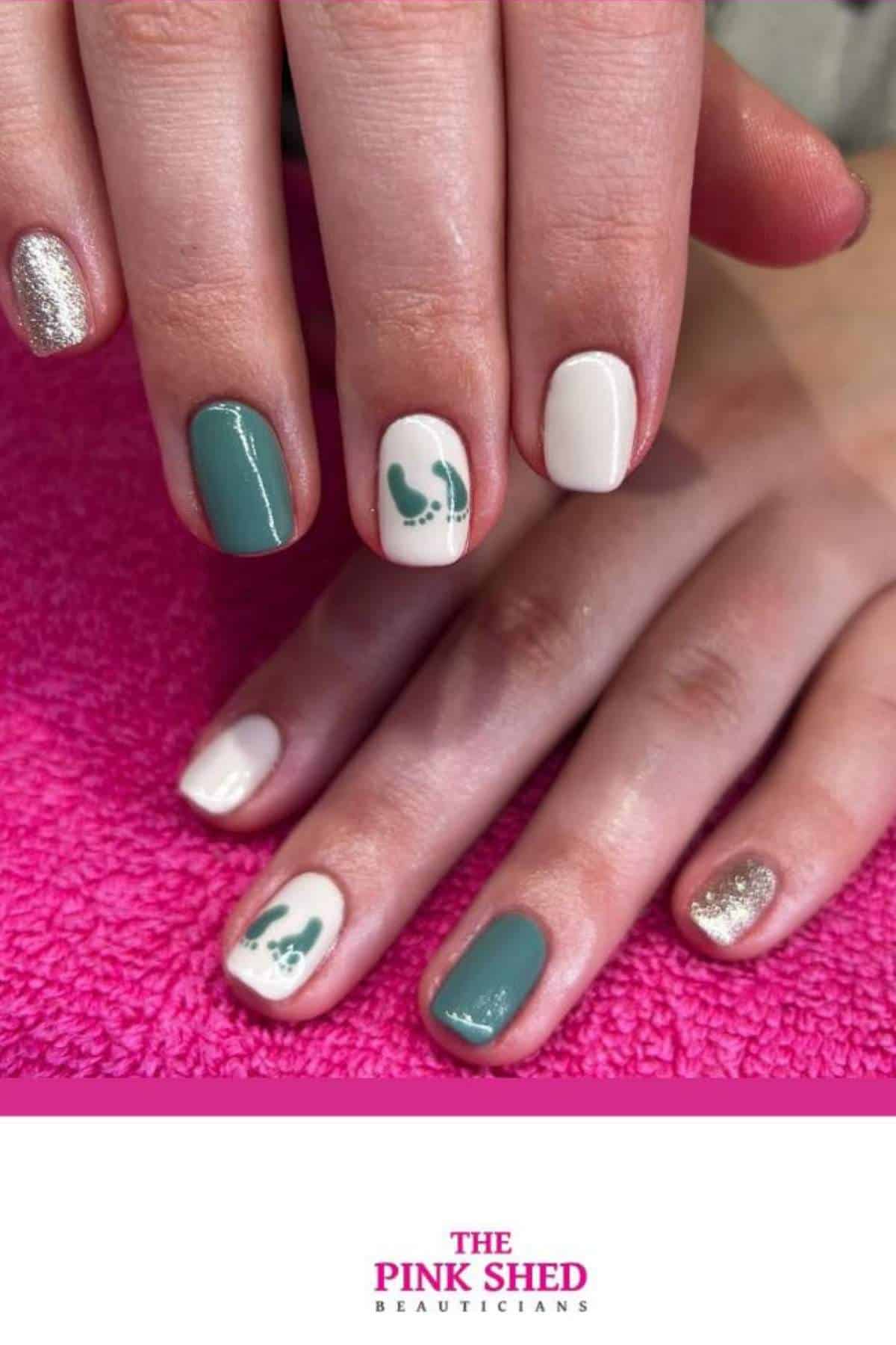 A hand with manicured nails in green, white, and gold polish, some nails featuring small green abstract designs, on a pink towel.