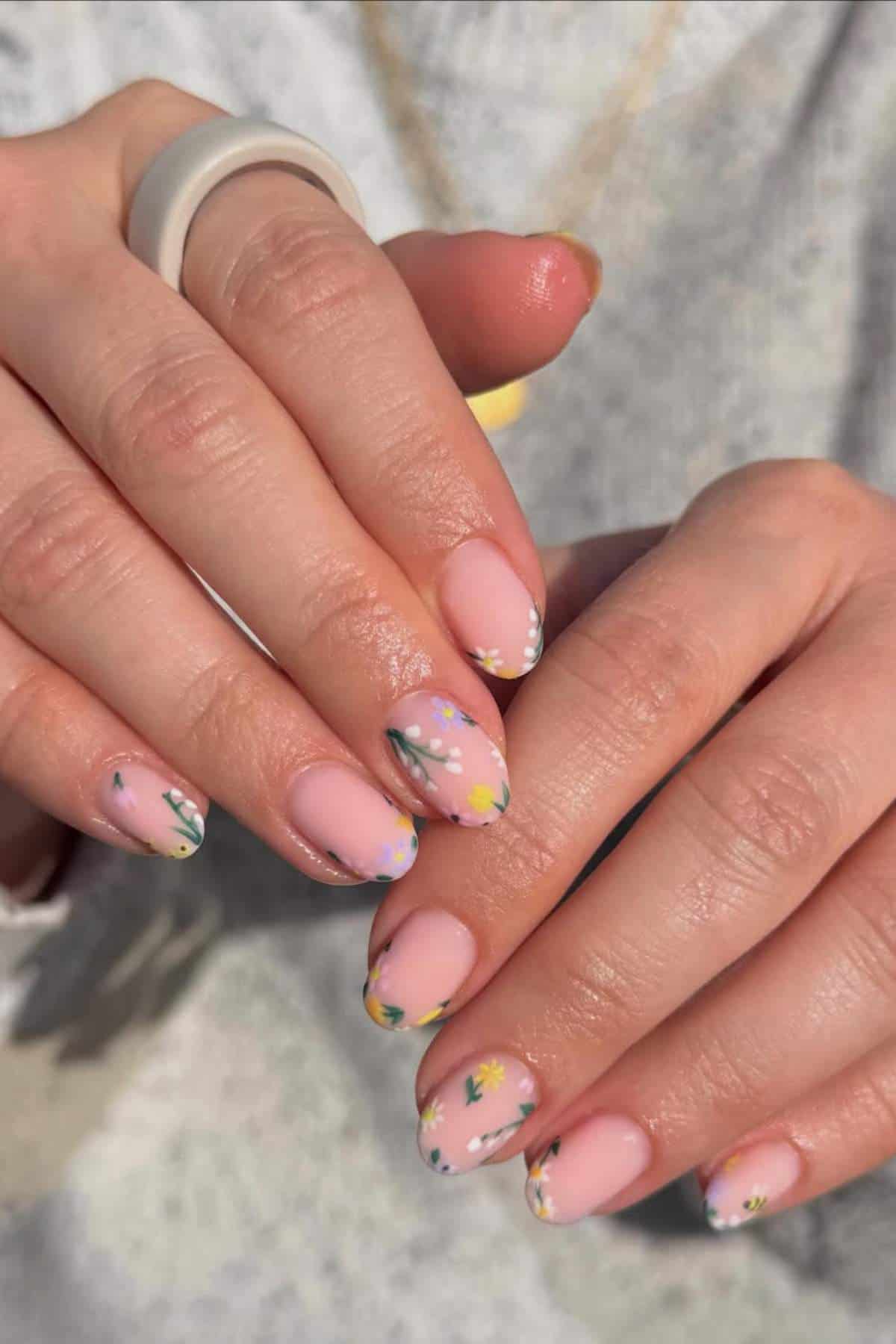 Close-up of hands with almond-shaped nails painted light pink and decorated with small, colorful floral designs and white dots.