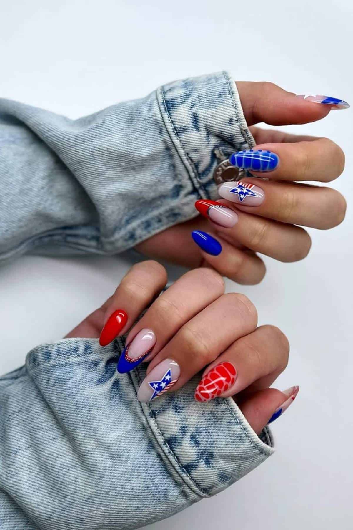 Hands with long, almond-shaped nails featuring red, blue, and nude tones with geometric patterns and star designs, visible through the sleeves of a light denim jacket.