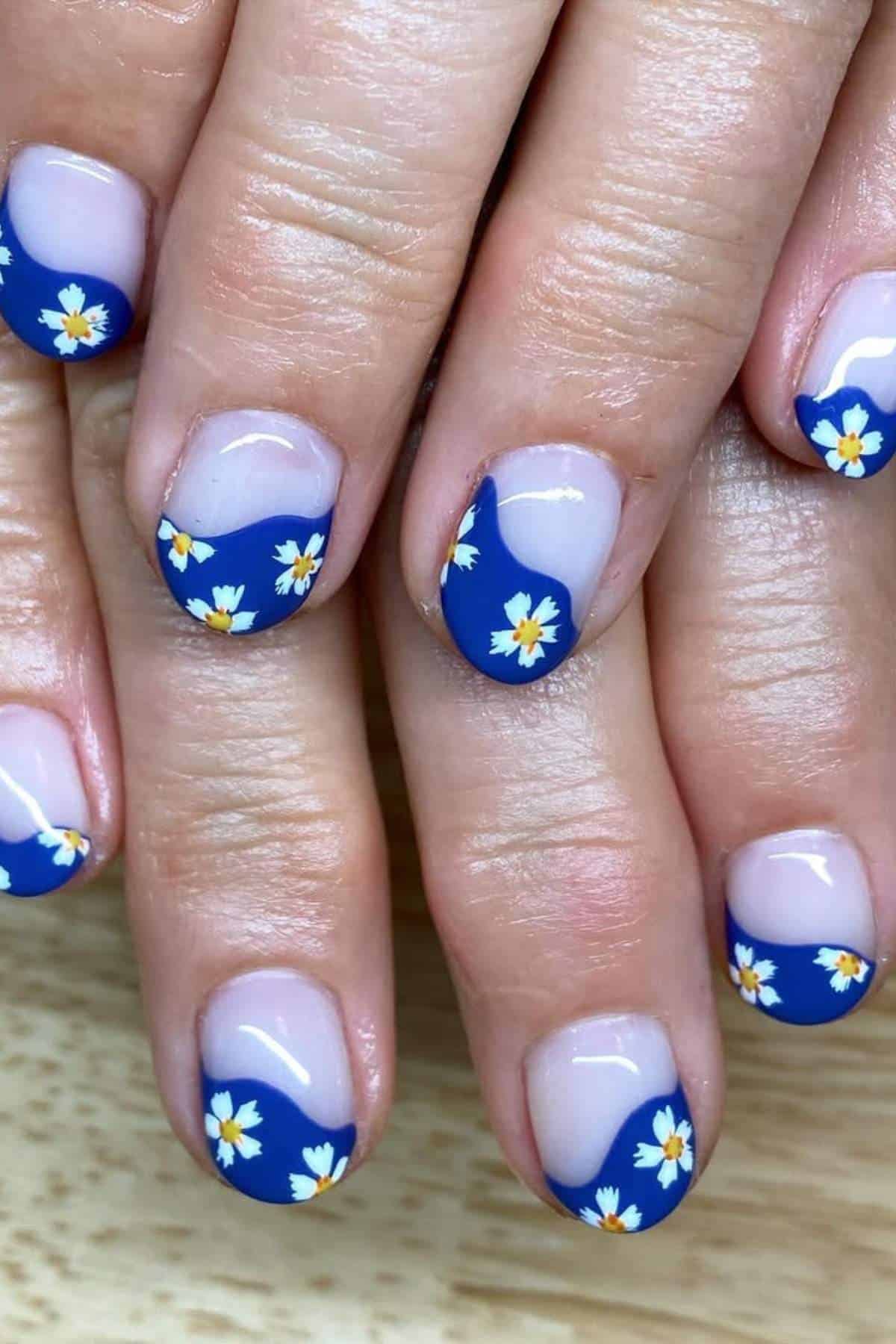 Close-up of fingernails with a blue French tip and small white daisy flower nail art design on a natural base color.