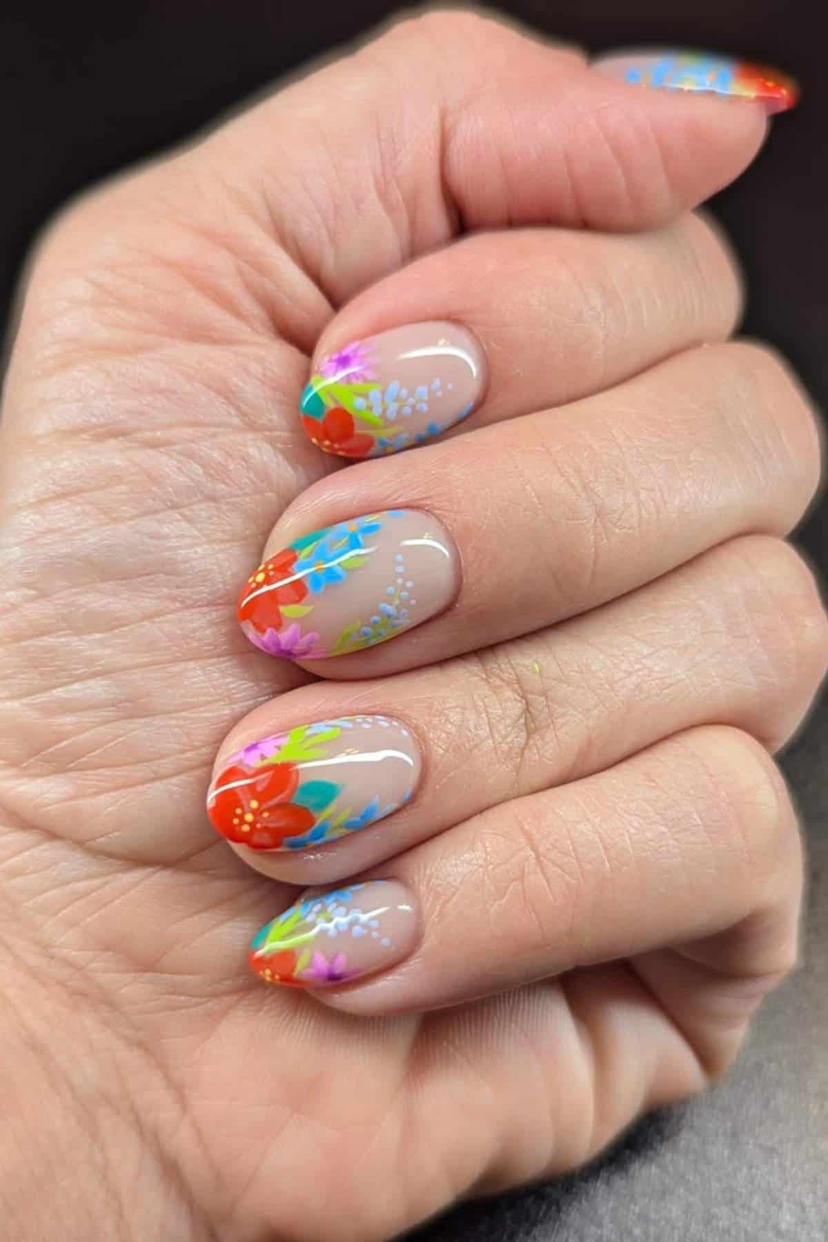 A hand with almond-shaped nails featuring colorful floral nail art on a nude base.