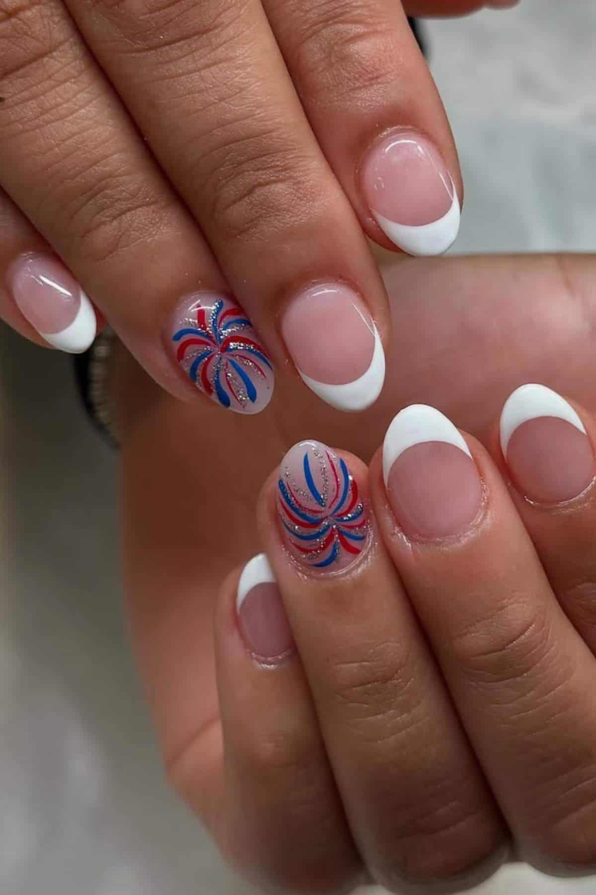 Hands with a French manicure; two nails feature red, blue, and silver swirl designs, while the rest have classic white tips on a natural base.