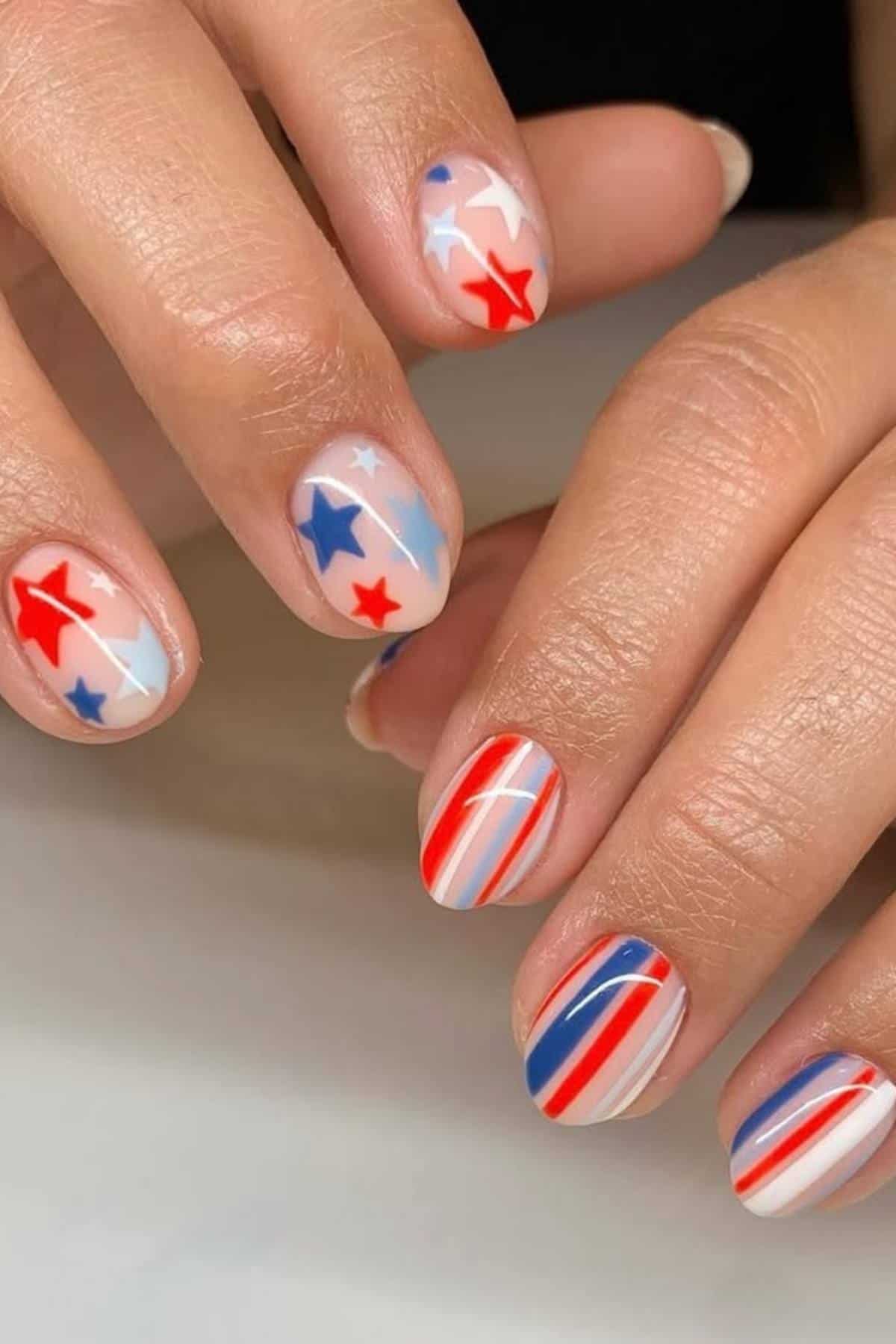 A hand with fingernails painted in red, white, and blue stripes and star patterns, resembling a patriotic or flag-inspired nail art design.