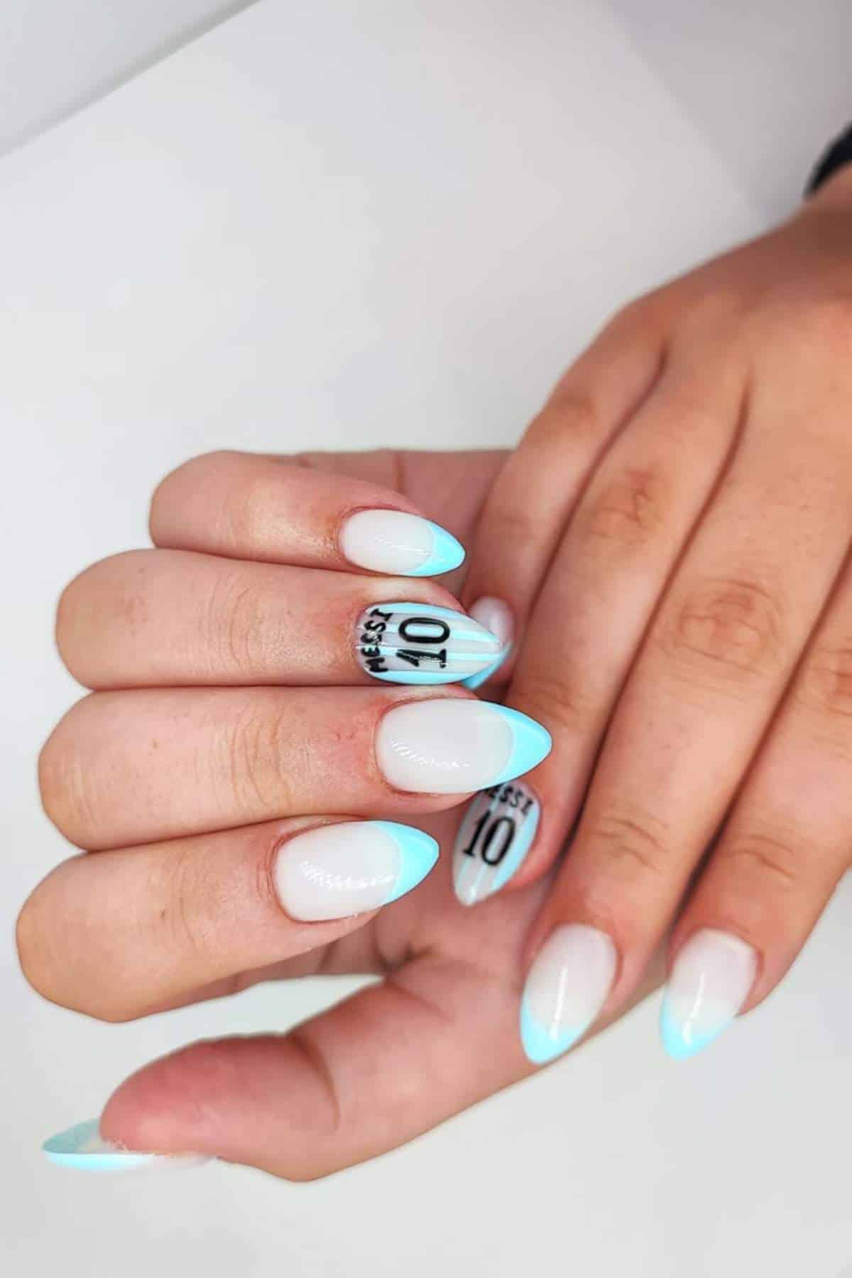 A hand with almond-shaped nails featuring a pale base, light blue tips, and black text reading "YES! 10" on two accent nails.