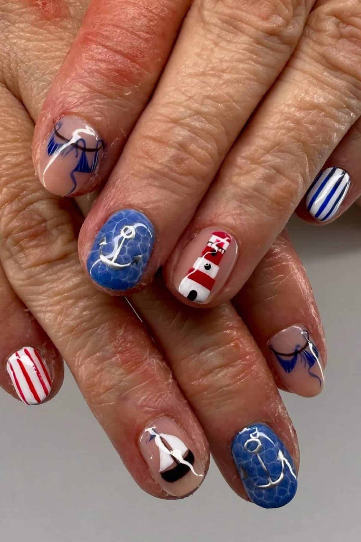 Close-up of hands with nautical-themed nail art featuring anchors, a lighthouse, and blue, red, and white stripes.