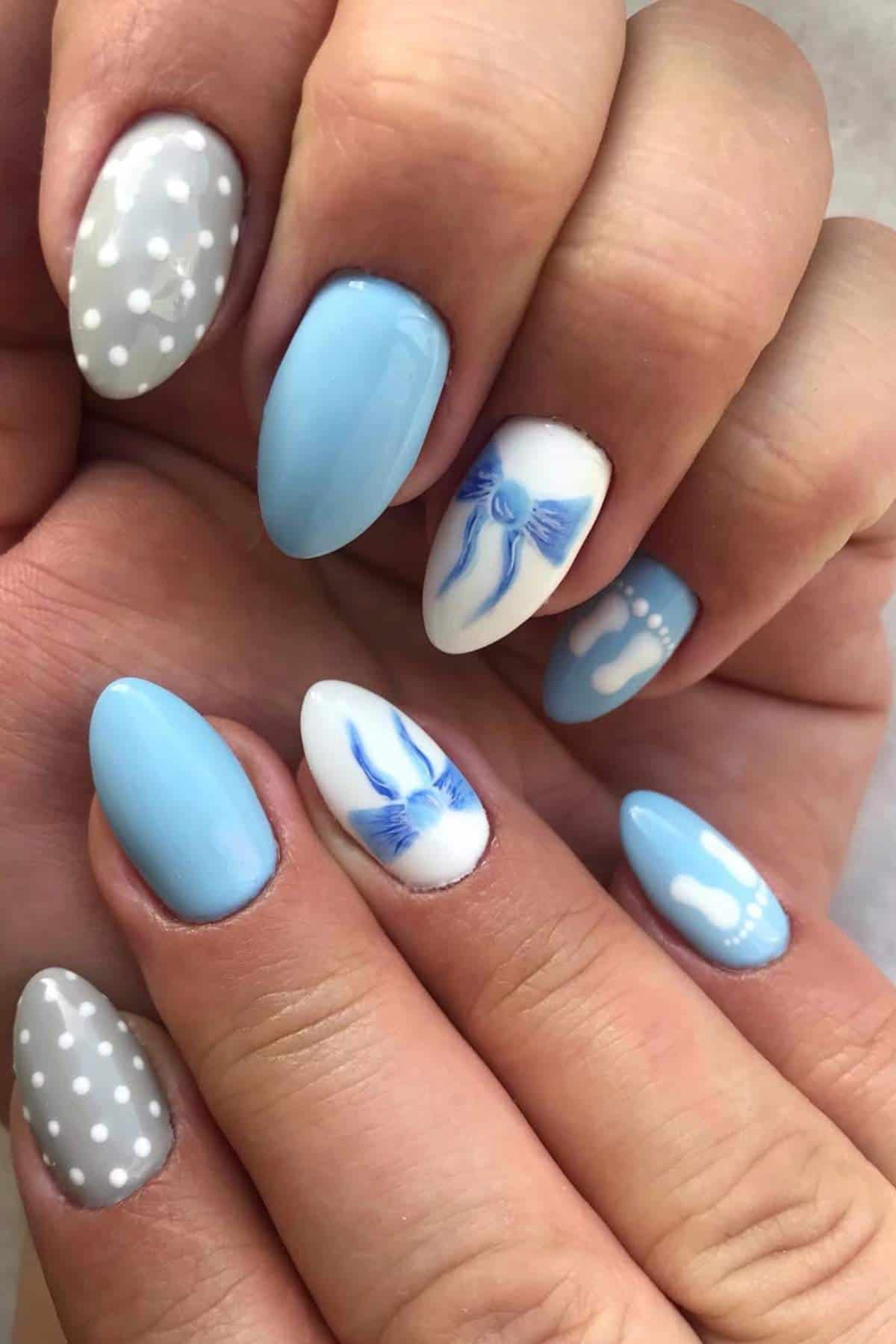 Hands with almond-shaped nails painted in light blue, white, and gray, featuring polka dots, blue bows, and decorative designs.