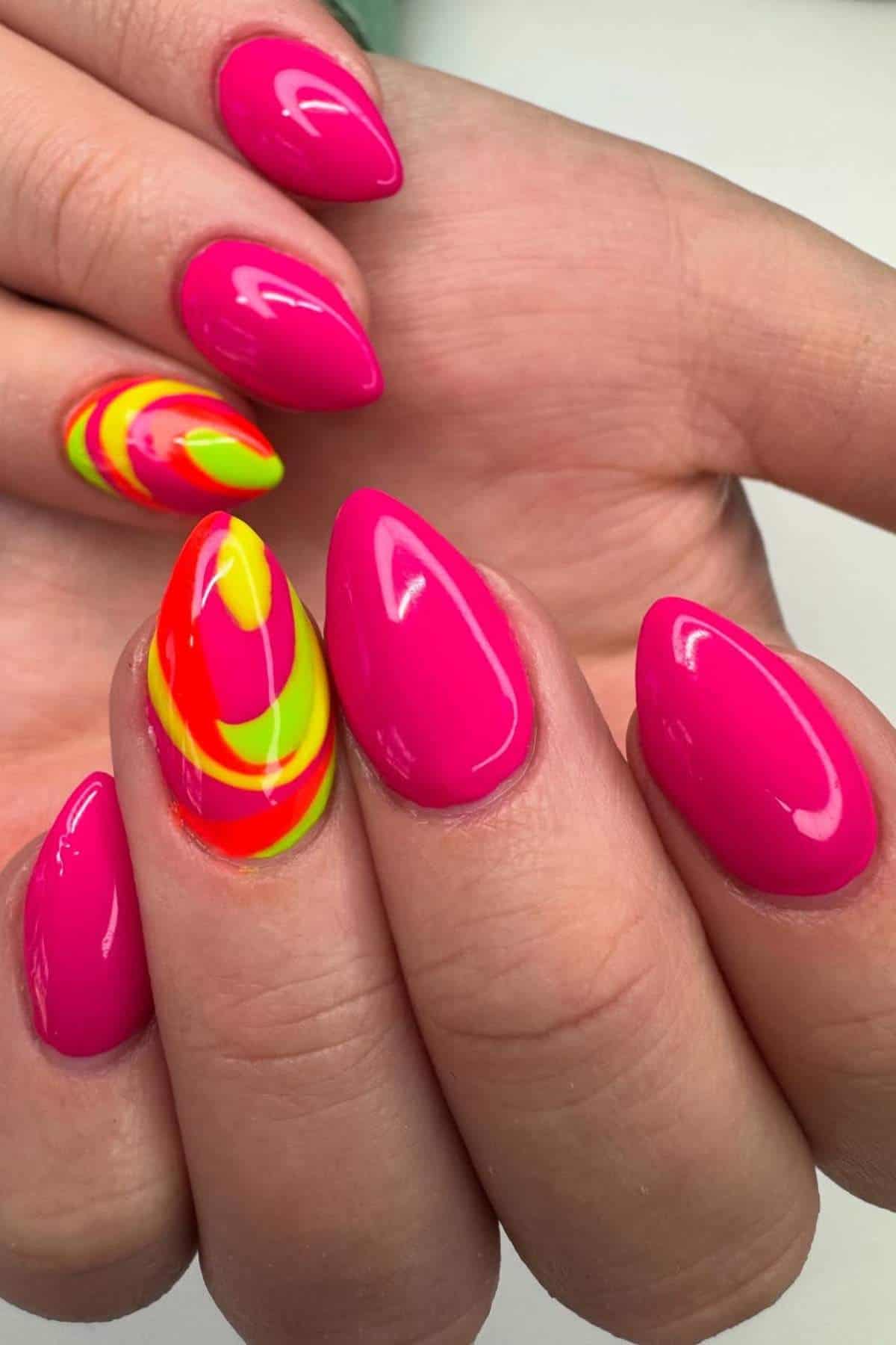 A hand with almond-shaped nails painted bright pink, with one accent nail featuring a neon yellow, green, and red swirl design.