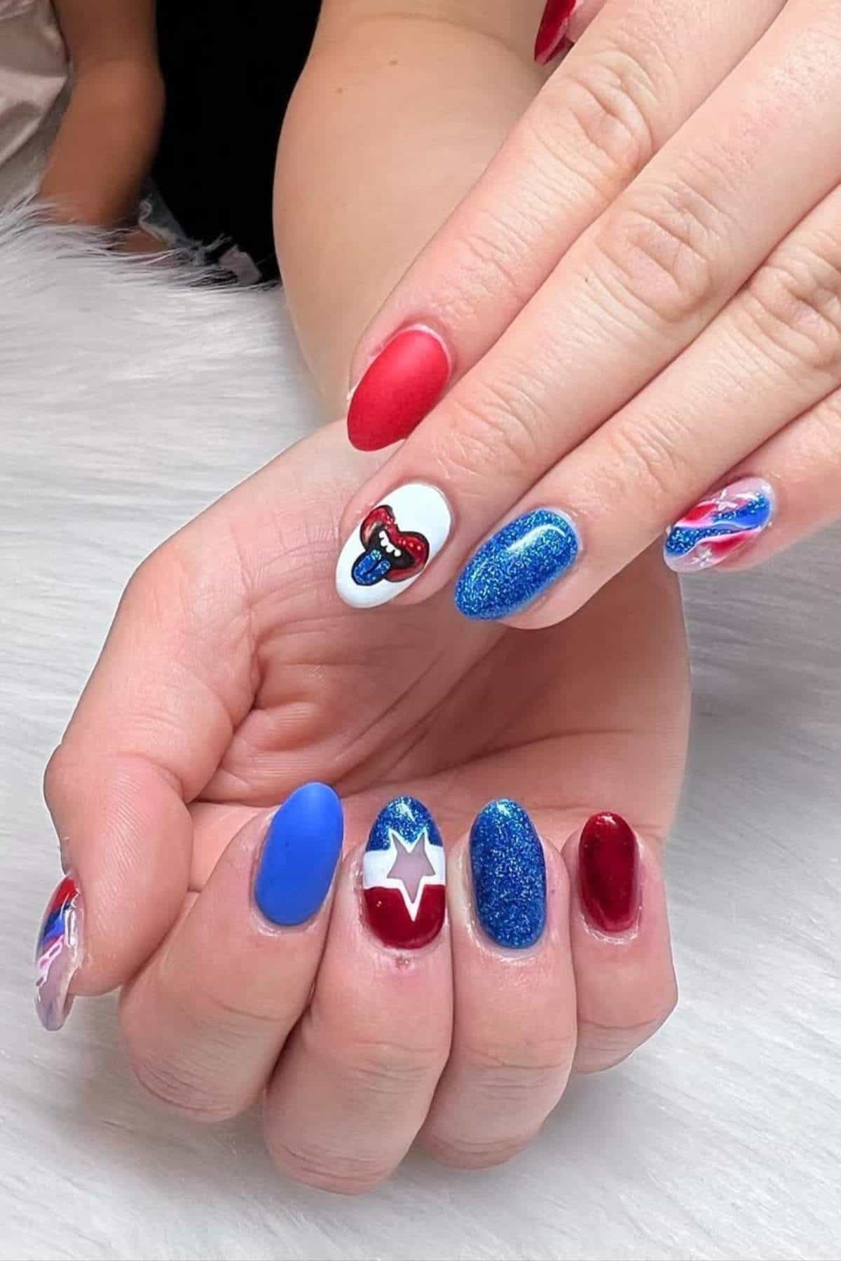 A hand with almond-shaped nails painted in red, blue, and white with glitter, stars, and heart designs, resting on a white surface.