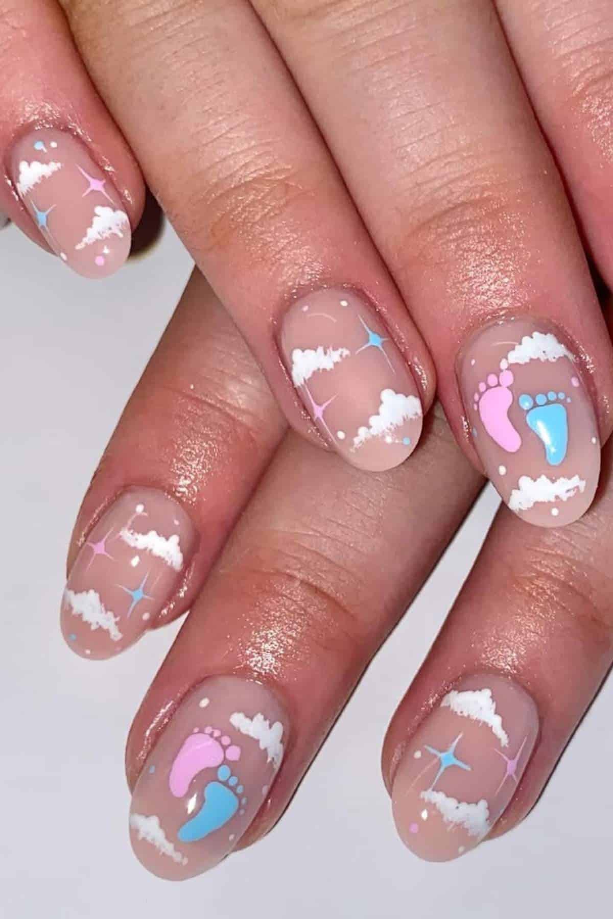 Close-up of hands with nails painted with clouds, pastel stars, and pink and blue baby footprint designs on a nude base.