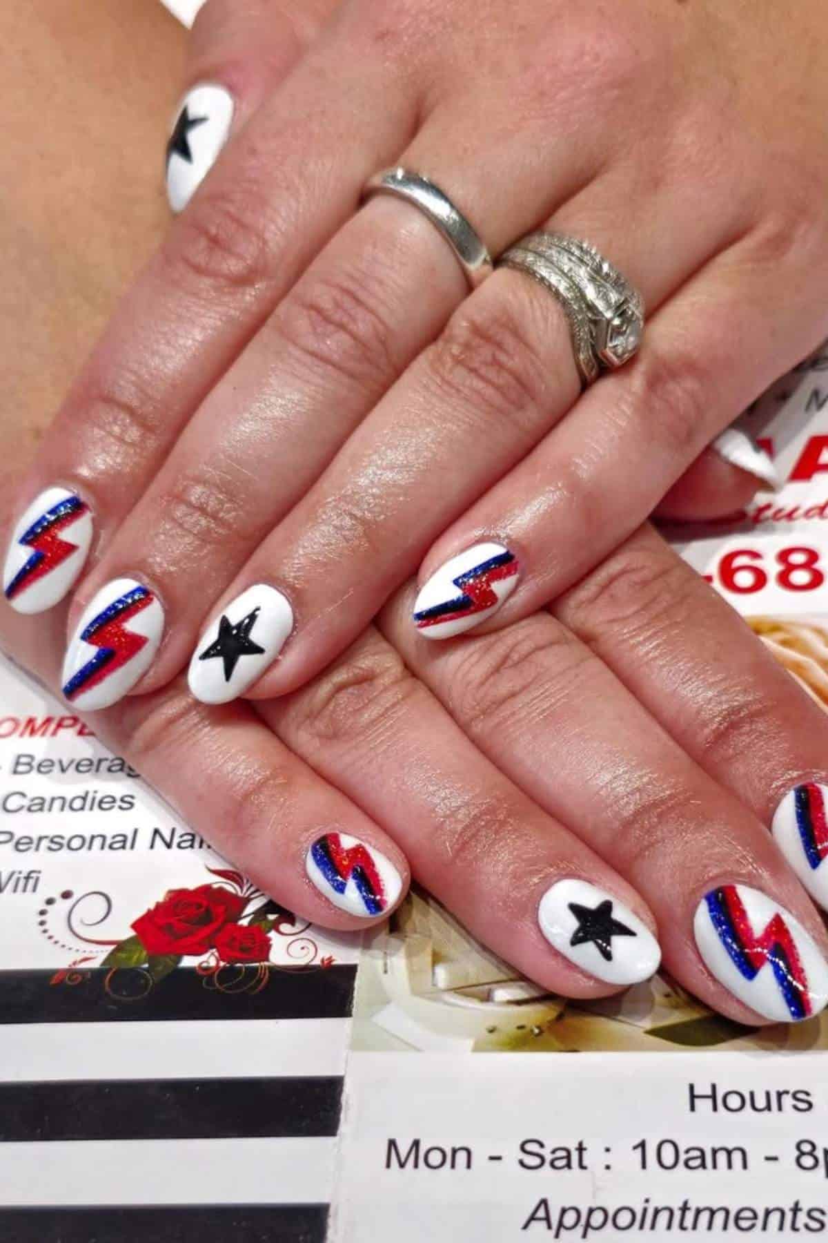 Hands with manicured nails featuring red and blue lightning bolts and black stars on a white background, resting on a printed surface.