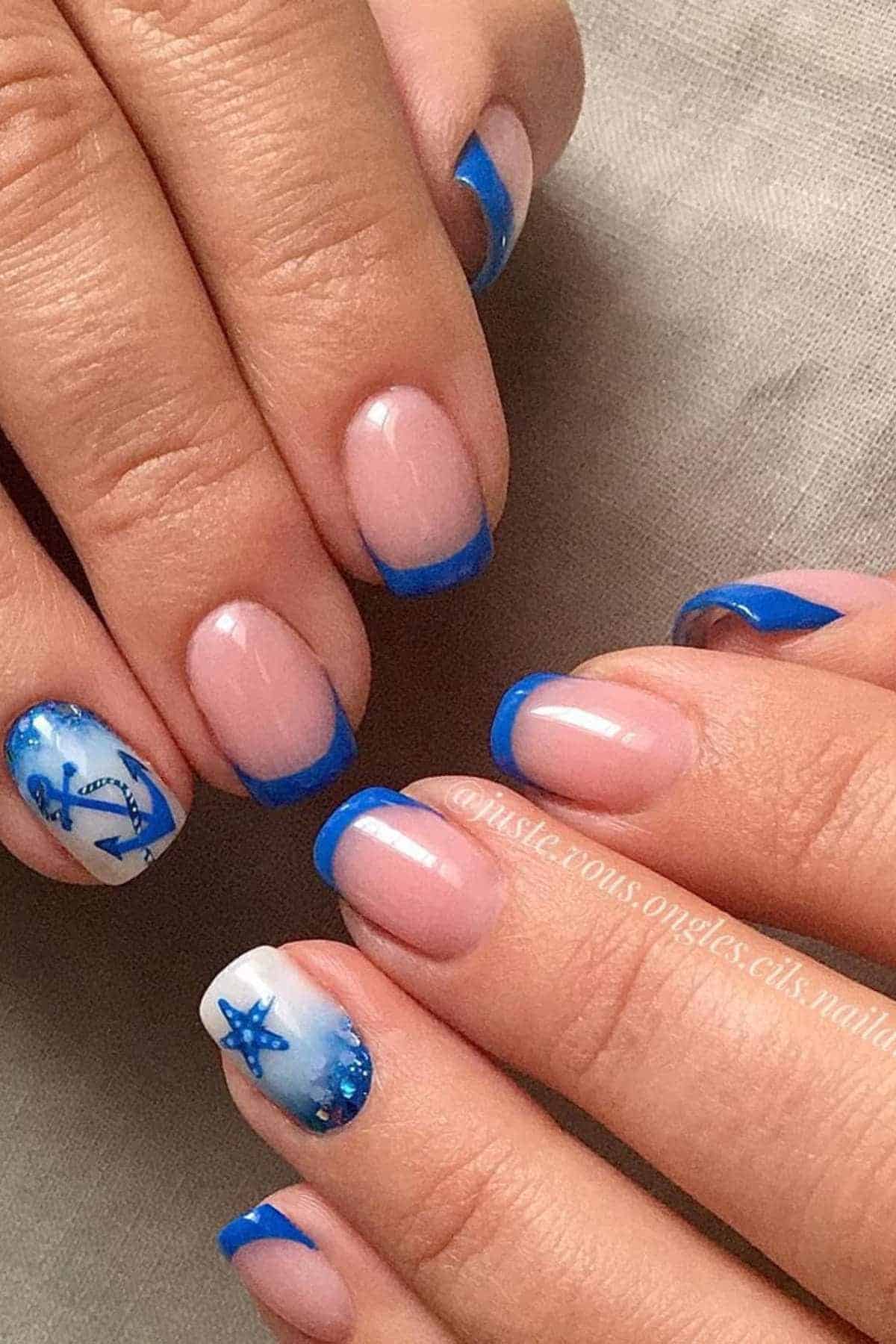 Hands with nails painted in a French manicure style with blue tips; some nails feature nautical designs like an anchor and a starfish.