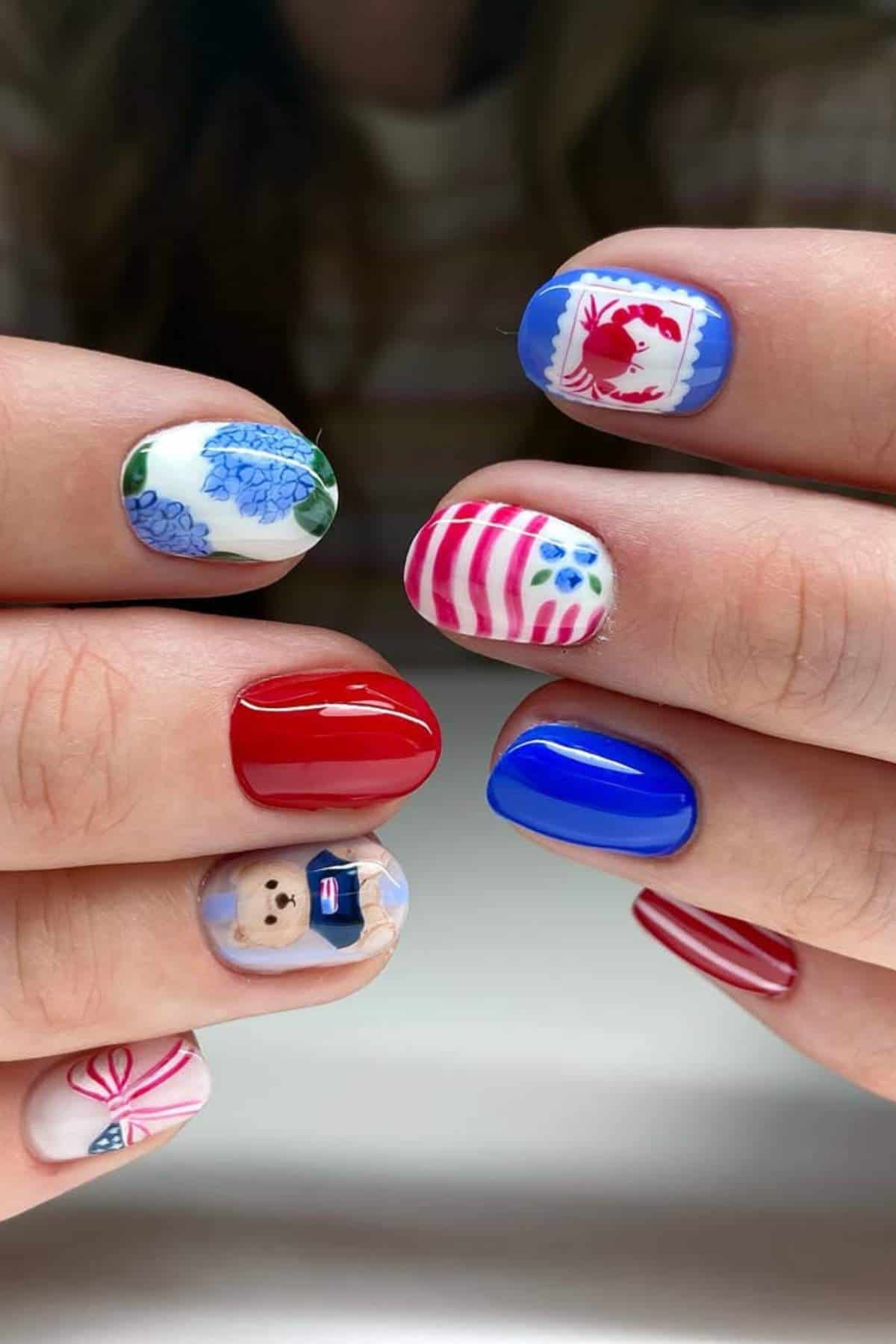 Close-up of hands with colorful nail art, featuring designs like flowers, stripes, a teddy bear, and a red fish, in red, blue, and white tones.