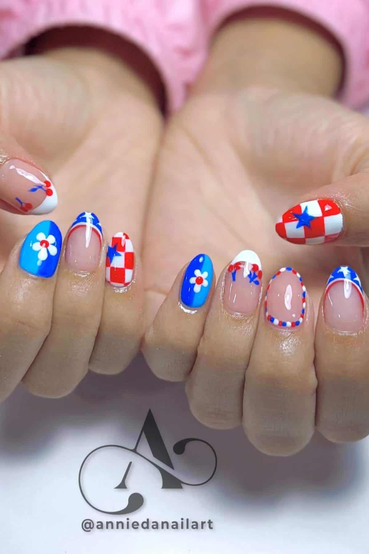 Hands with almond-shaped nails painted in a red, white, and blue patriotic theme, featuring stars, flowers, and checkerboard patterns.