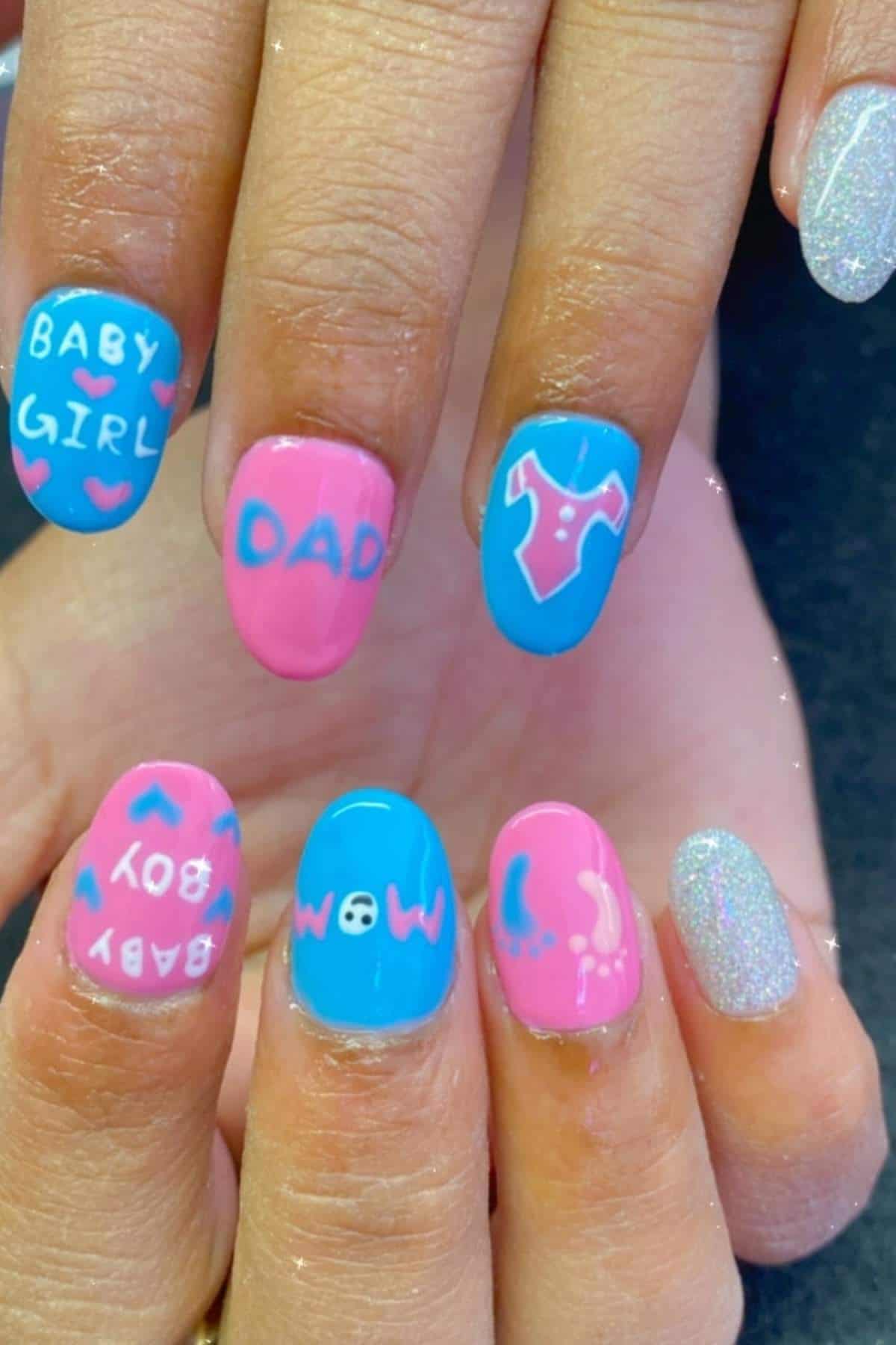 Close-up of hands with brightly painted nails in pink, blue, and silver, featuring words like "BABY GIRL," "DAD," "BABY BOY," and baby-themed designs.