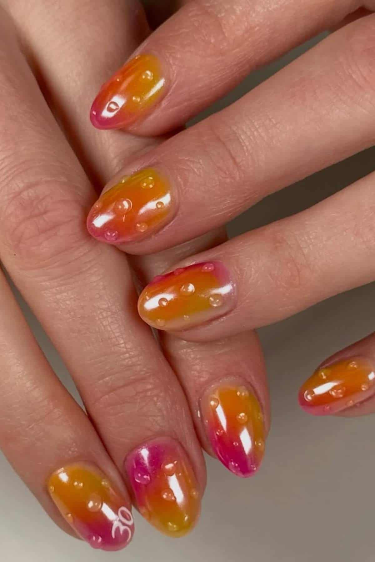 Hands with almond-shaped nails painted in a glossy orange, pink, and yellow gradient design, featuring small raised dots and the number "30" on one nail.