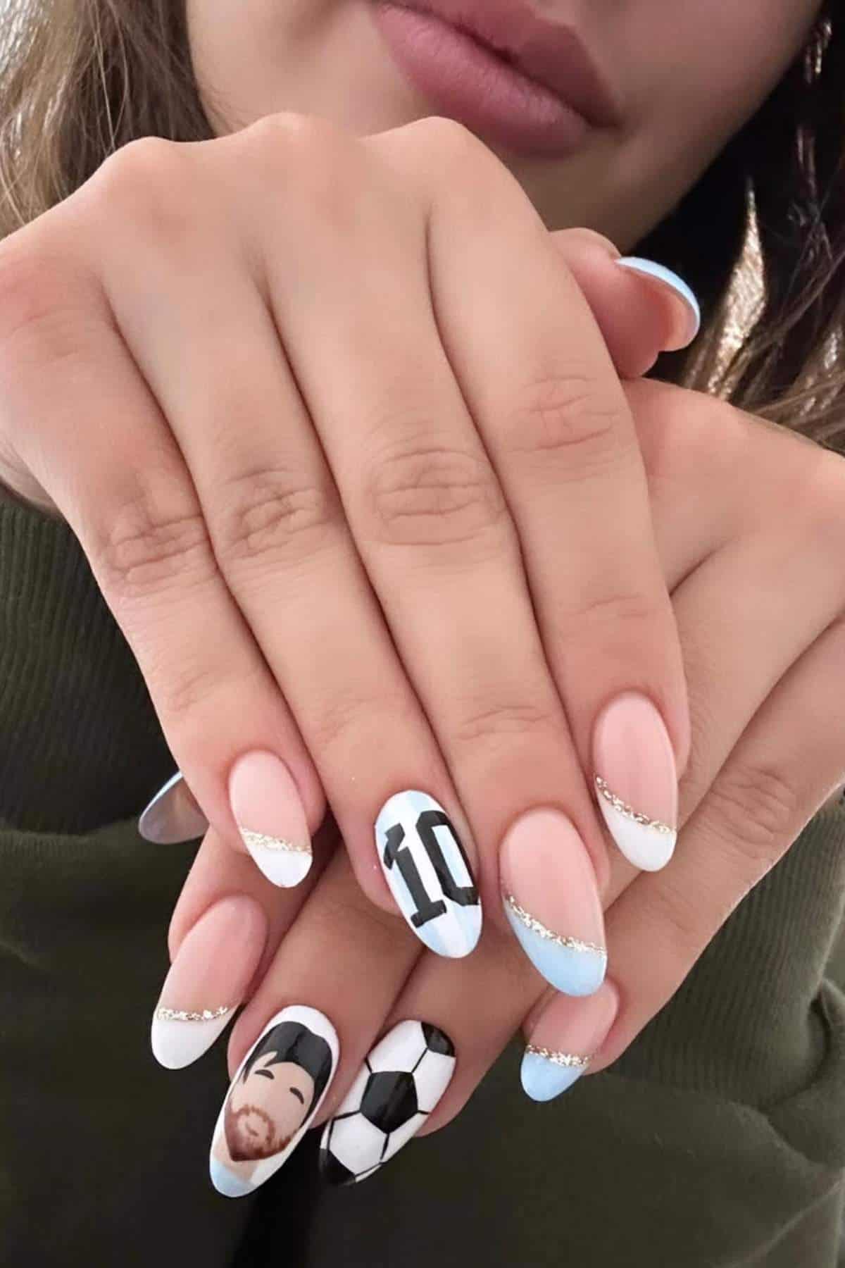 Close-up of a person's manicured hands with light blue, white, and nude nails featuring a soccer ball, the number 10, and a face illustration as nail art.