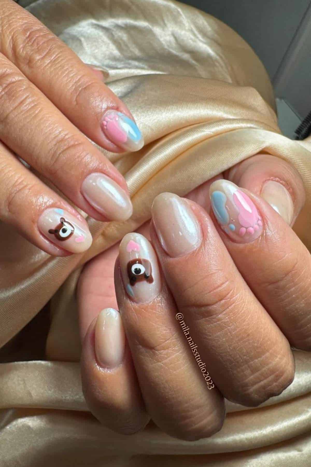Hands with manicured nails featuring pastel pink, blue, and nude abstract designs, with some nails decorated with small bear faces.