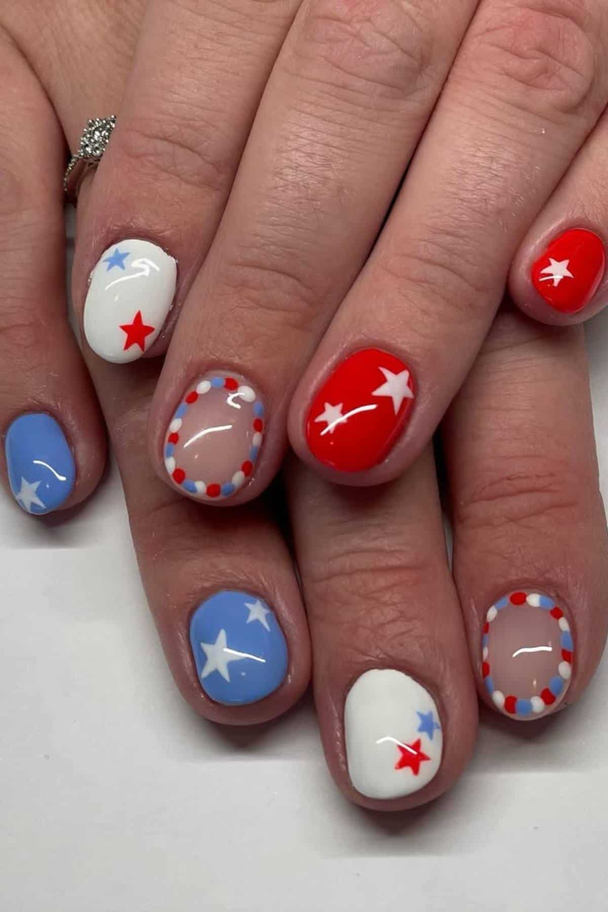 Hands with manicure featuring red, white, and blue nail polish, star designs, and dotted borders, inspired by a patriotic or American flag theme.