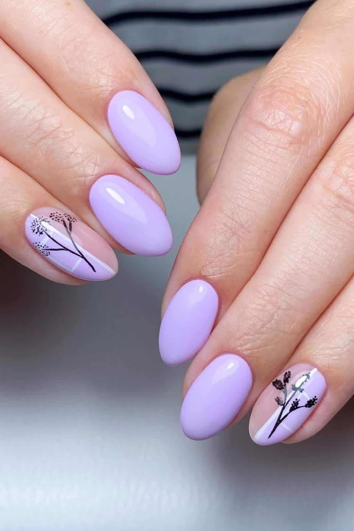 Hands with oval-shaped lavender nails; two accent nails feature delicate black botanical line art. A striped shirt is visible in the background.