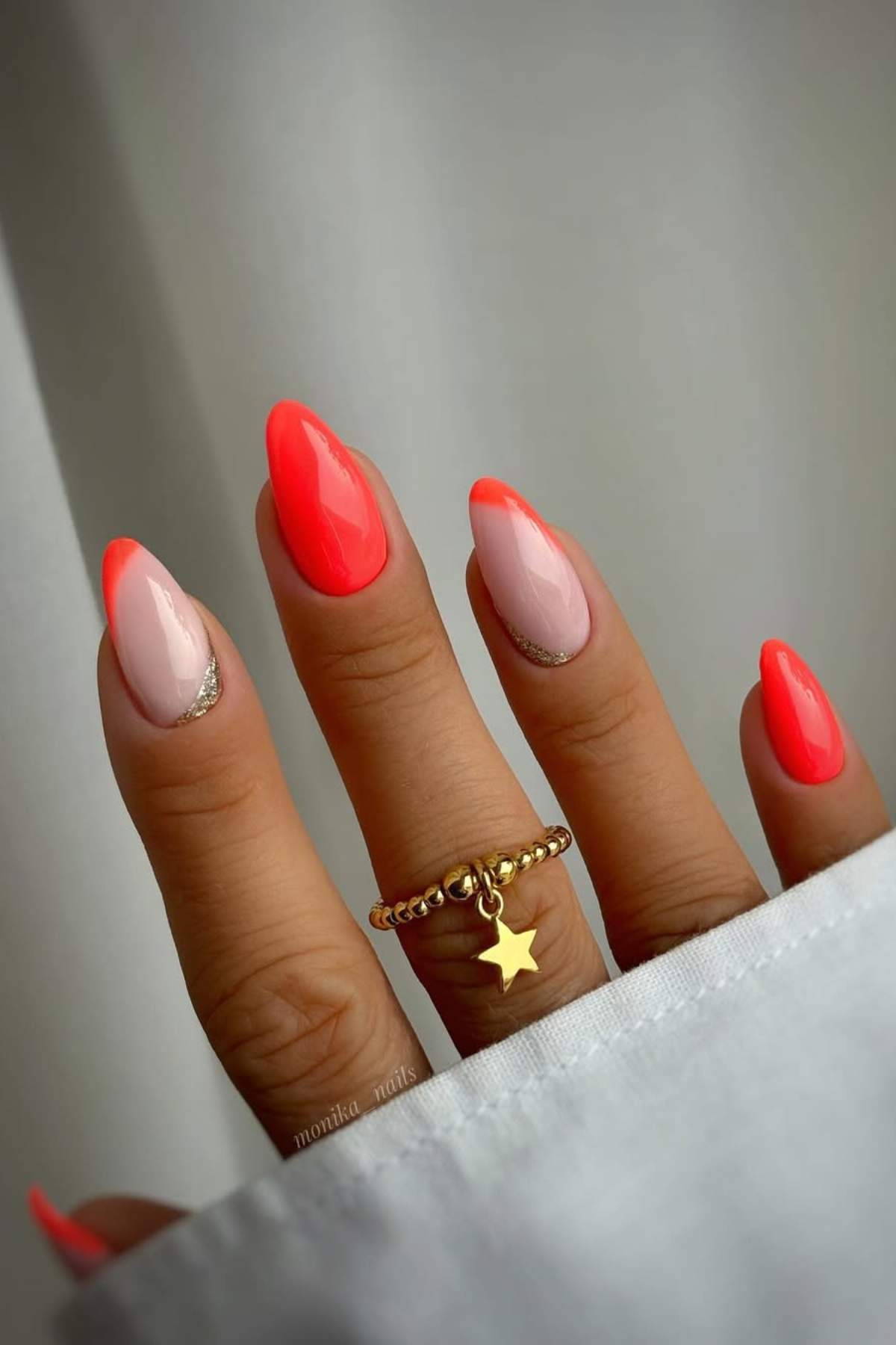 A hand with almond-shaped nails featuring a bright neon pink and nude French tip design, accented with a gold star ring on the finger.