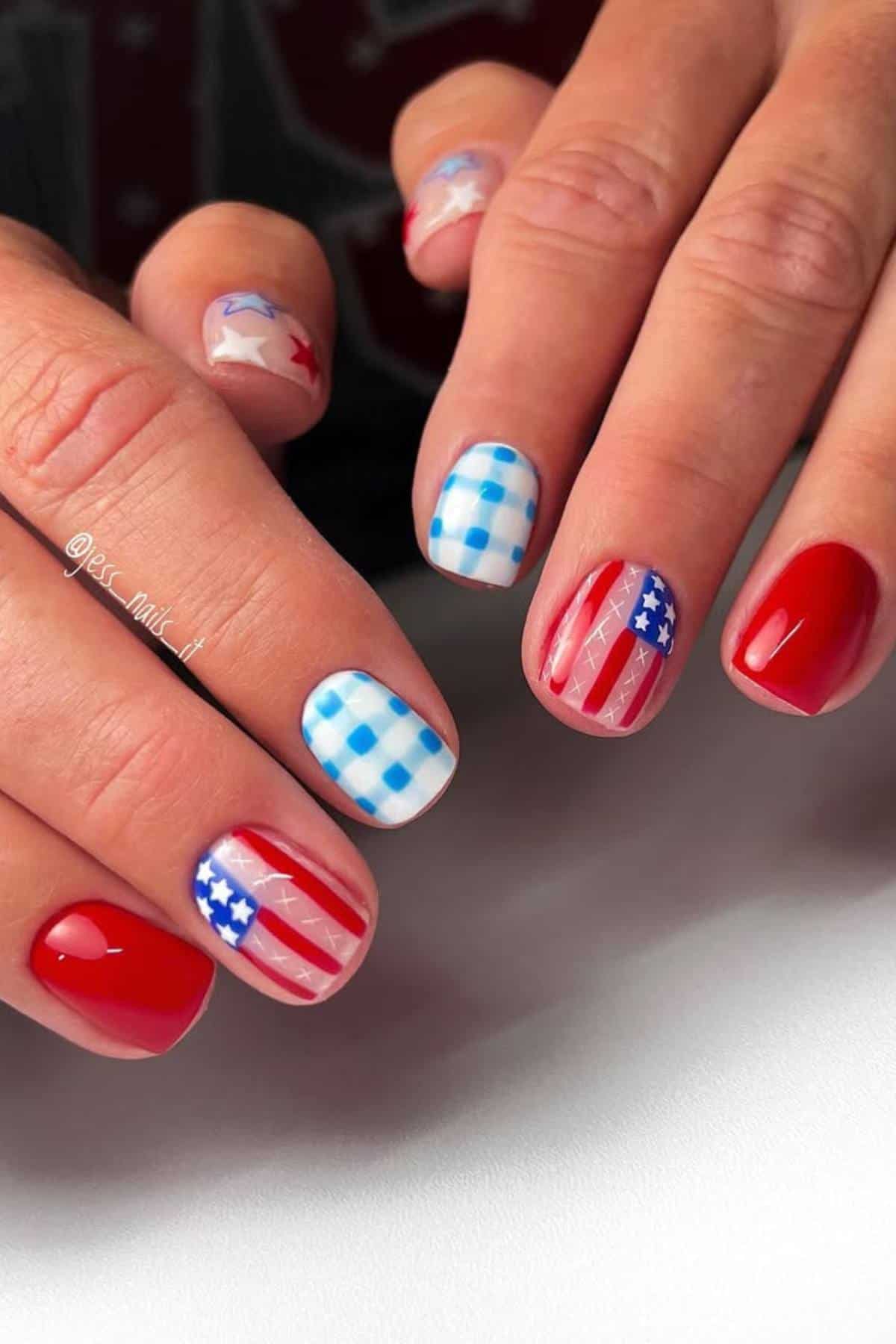 Hands with manicured nails featuring red polish, blue and white checkered pattern, American flag design, and red and blue stars on a light background.