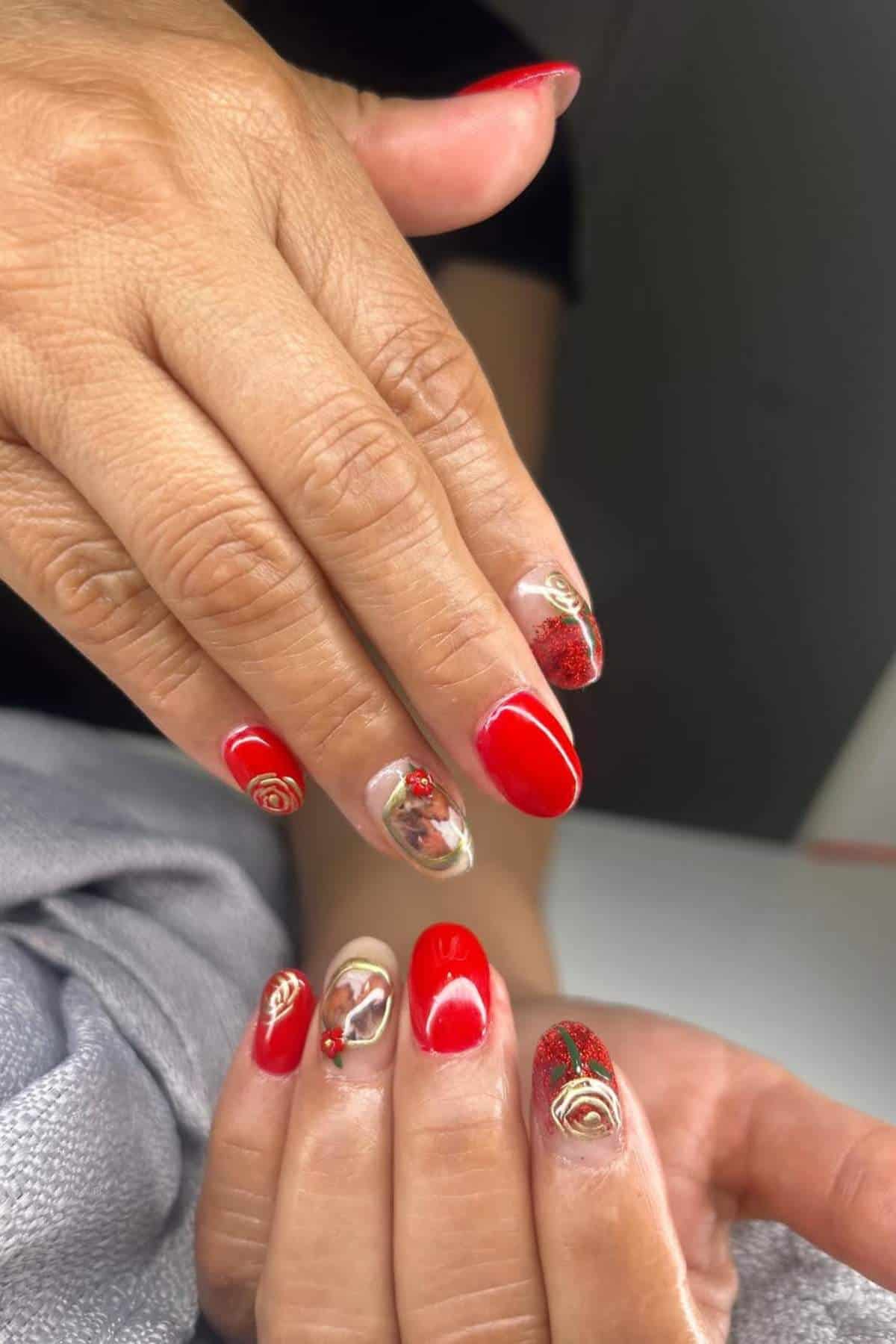Close-up of hands showing red manicured nails with gold and floral nail art accents on some fingers.