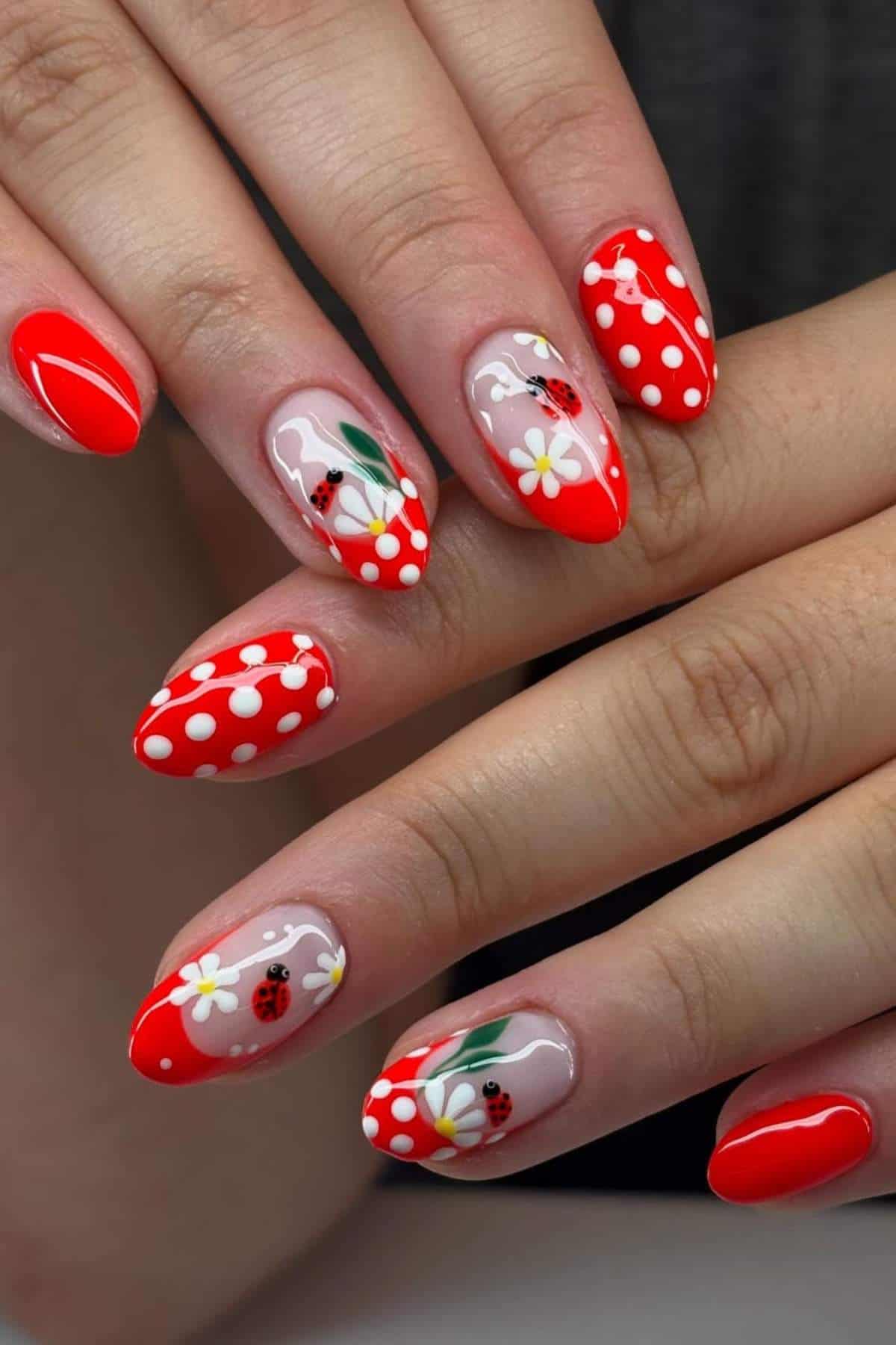 Hands with almond-shaped nails painted red with white polka dots, daisy flowers, and ladybug designs.