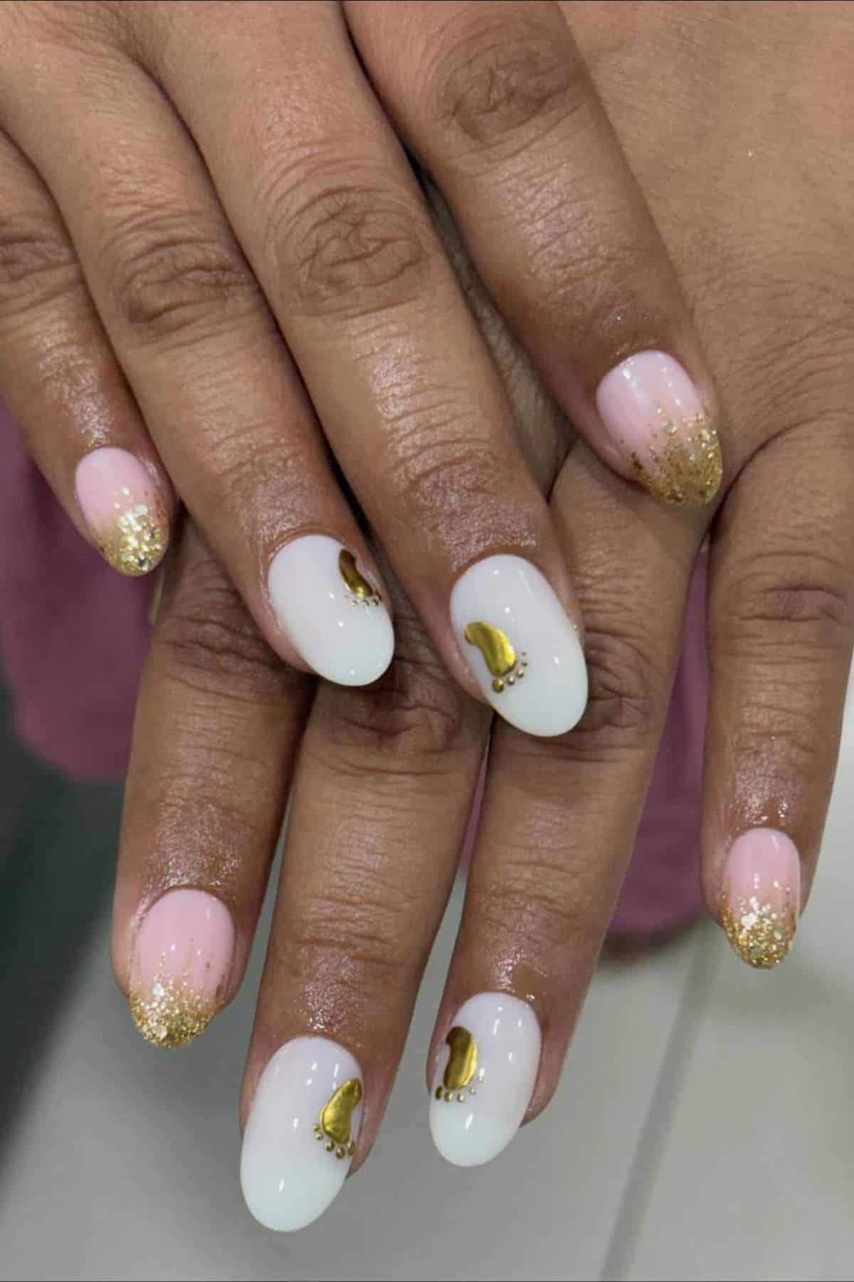 Hands with almond-shaped nails featuring pink and white polish, gold glitter tips, and gold crescent moon designs on the ring and middle fingernails.