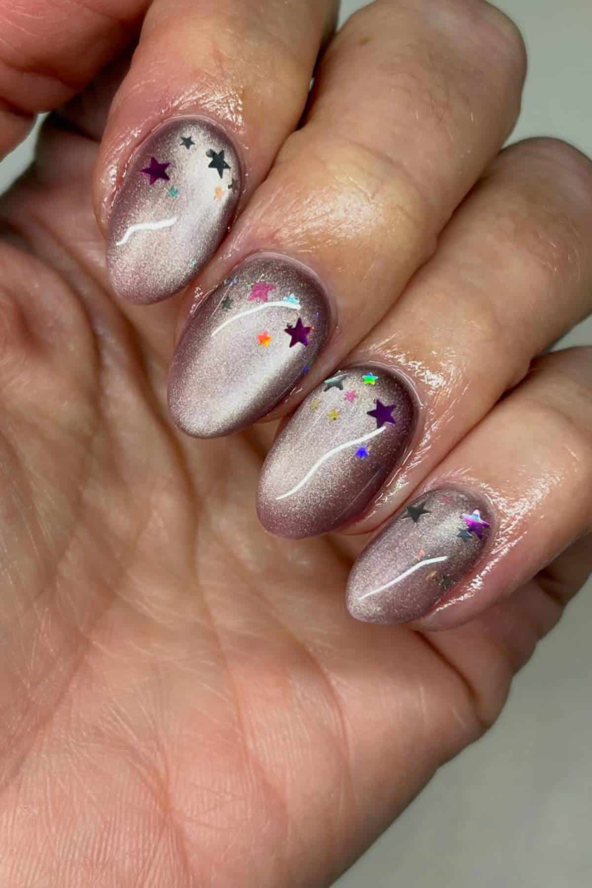 A hand with shimmery mauve nail polish, each nail decorated with small, colorful star-shaped sequins.