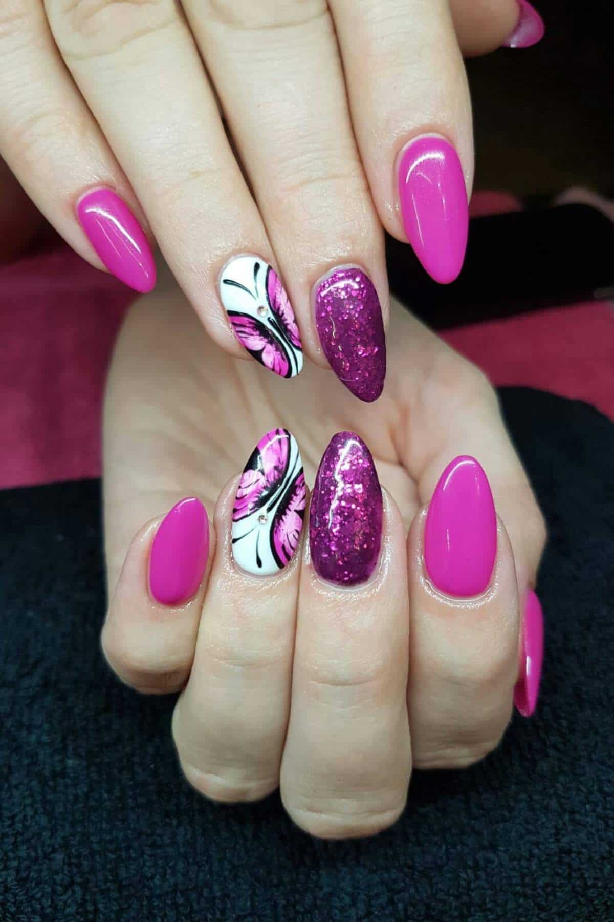 Hands with almond-shaped nails painted pink, featuring glitter on one nail and a butterfly wing design in pink, black, and white on another nail.