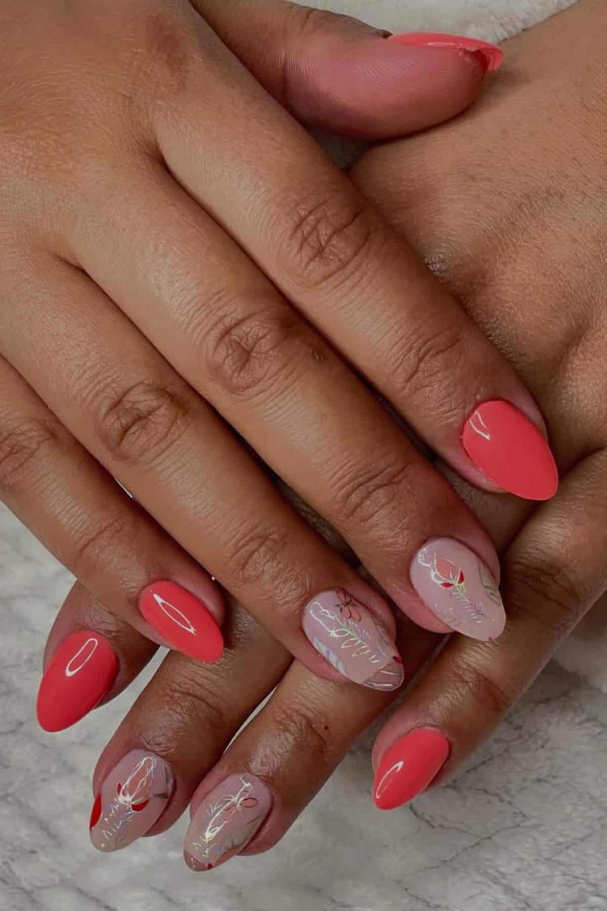 Hands with almond-shaped nails, painted in bright coral and nude shades, with some nails featuring delicate white and gold leaf designs.