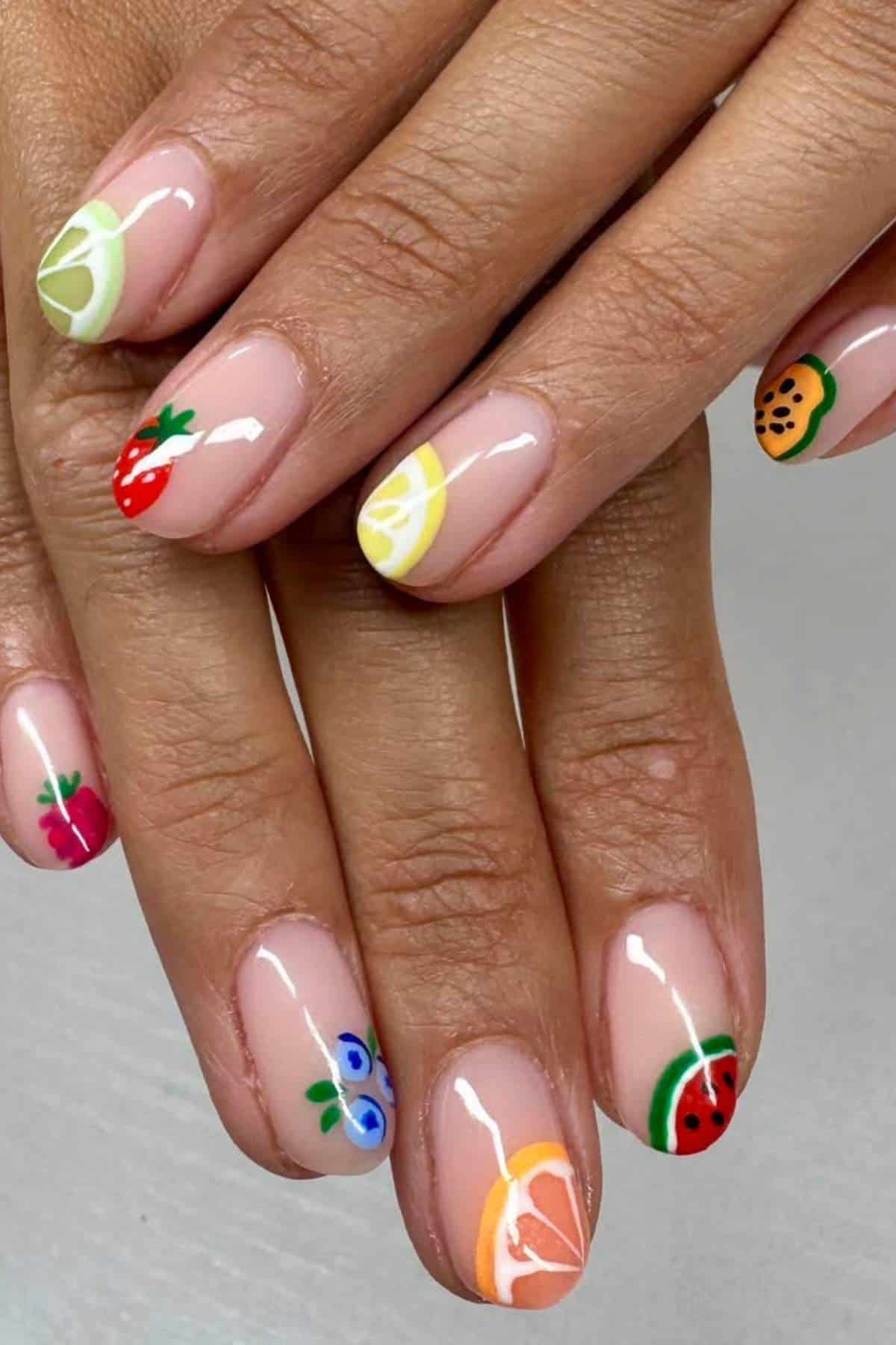 Hands with manicured nails painted with various colorful fruit designs, including lemon, strawberry, watermelon, orange, cherry, blueberry, and kiwi.
