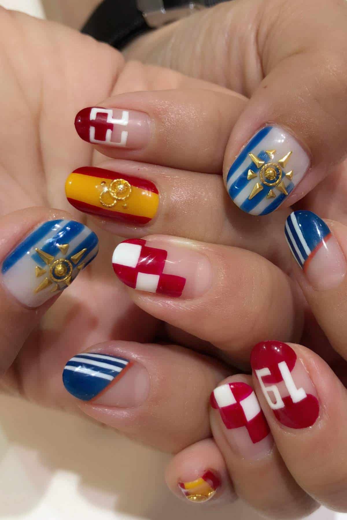 Close-up of hands with nautical-themed nail art featuring blue, red, white, and yellow colors, anchor and wheel decorations, and patterns resembling flags and numbers.