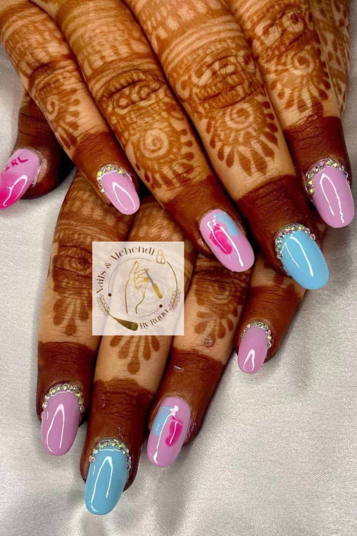 Hands with henna designs and manicured nails in pastel pink and blue colors, each nail decorated with rhinestones near the cuticles.