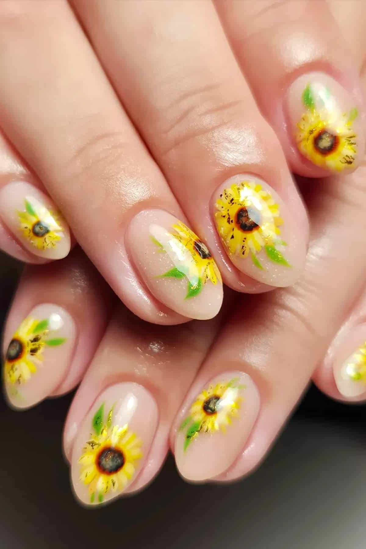 Close-up of fingernails with a nude base polish and hand-painted sunflower designs on each nail.