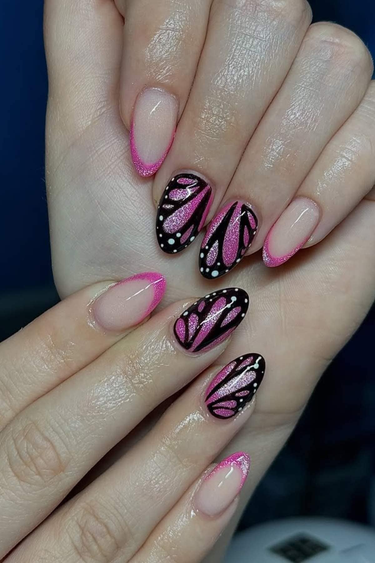 Hands with almond-shaped nails featuring pink French tips and butterfly wing designs with black and white accents on two nails.