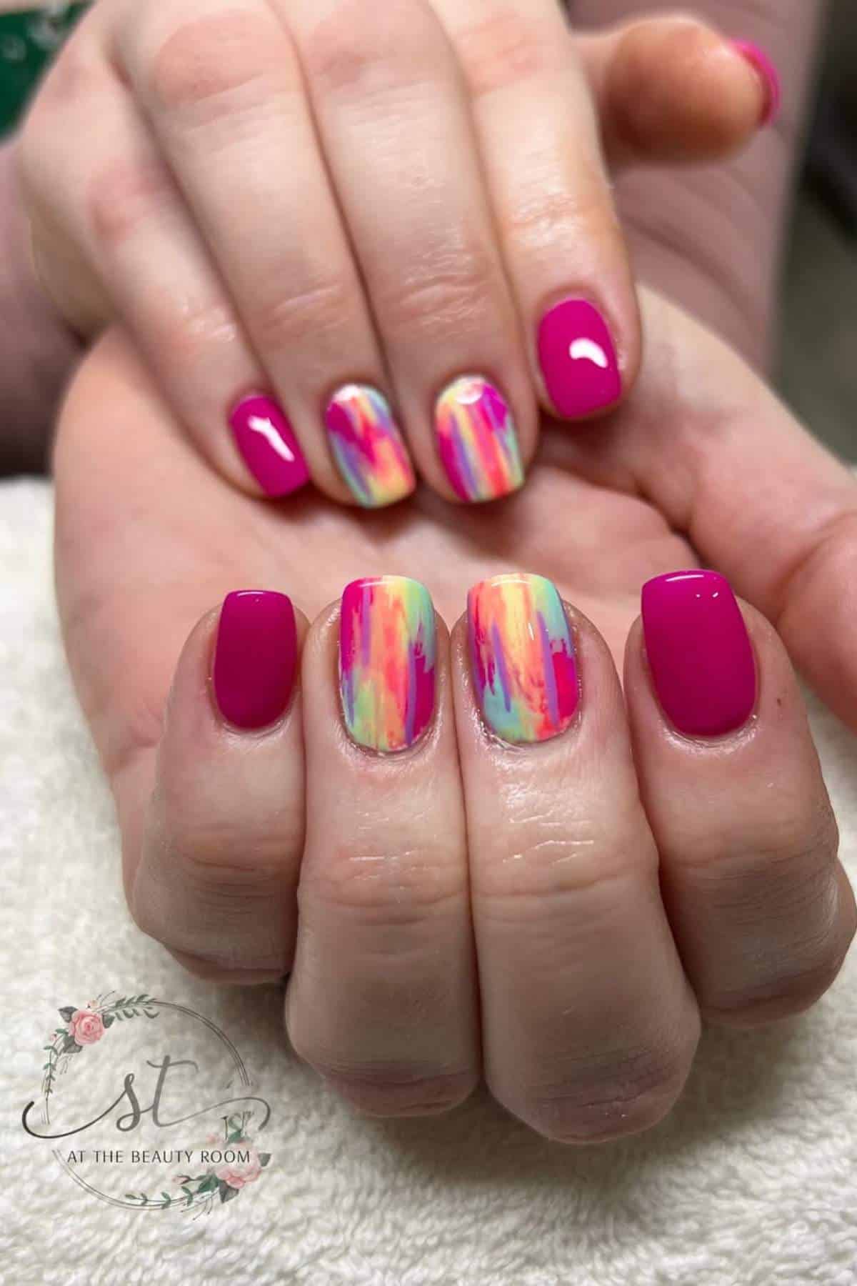 Hands with short, square-shaped nails featuring bright pink polish and two accent nails with a colorful, abstract brushstroke design.