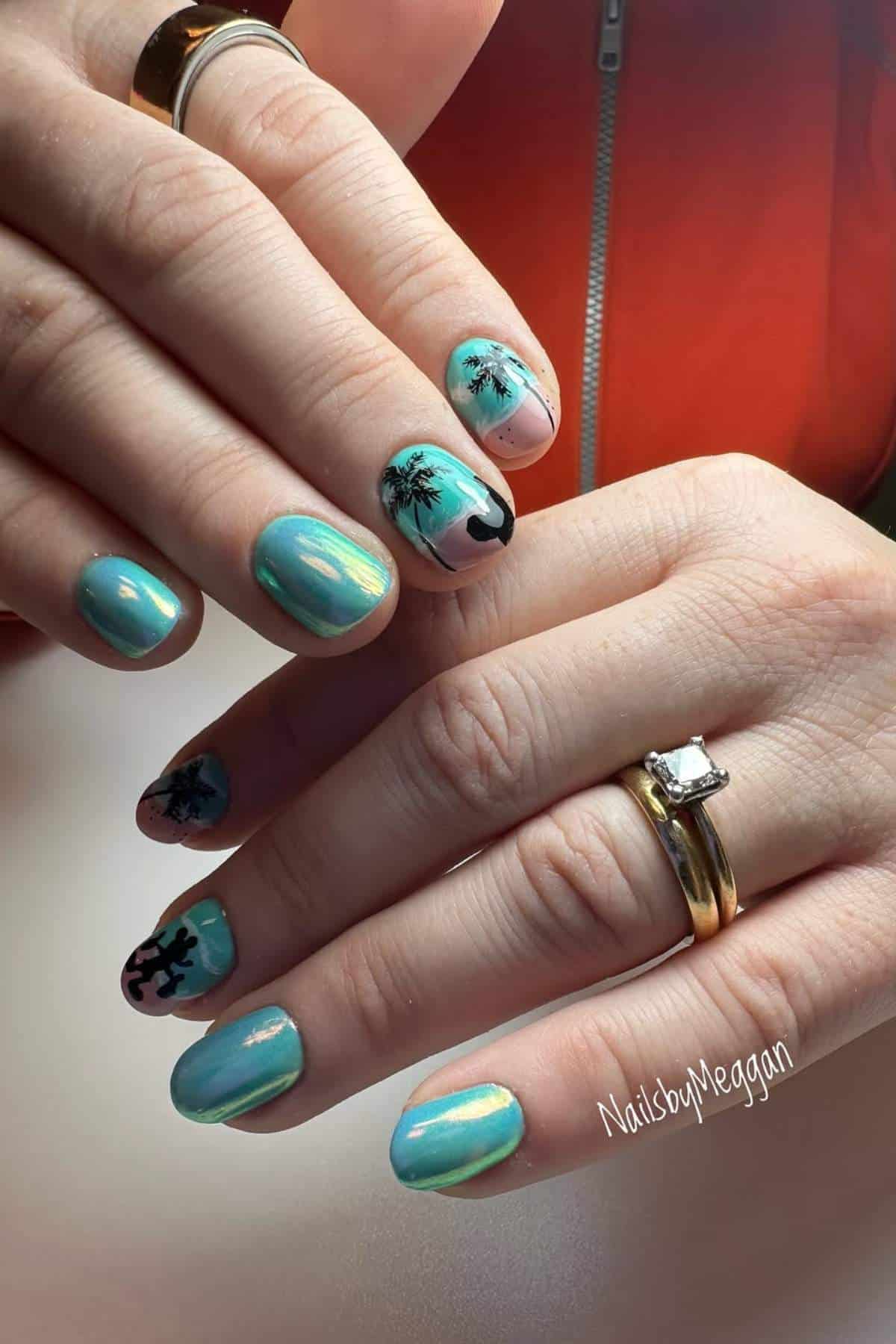 Hands with blue and teal iridescent nail polish, some nails featuring black palm tree and wave designs. Person is wearing a gold ring with a square-cut stone and a gold band.