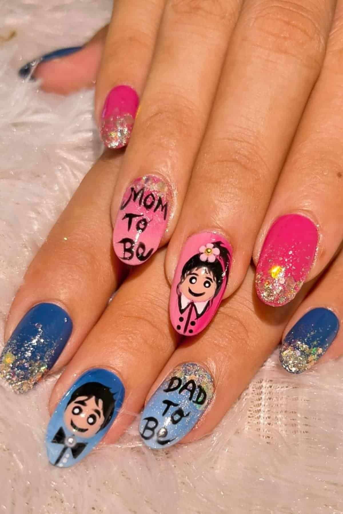 Close-up of hands with colorful nail art featuring cartoon faces and text reading "MOM TO BE" and "DAD TO BE" on the middle and ring fingernails, with glitter accents.