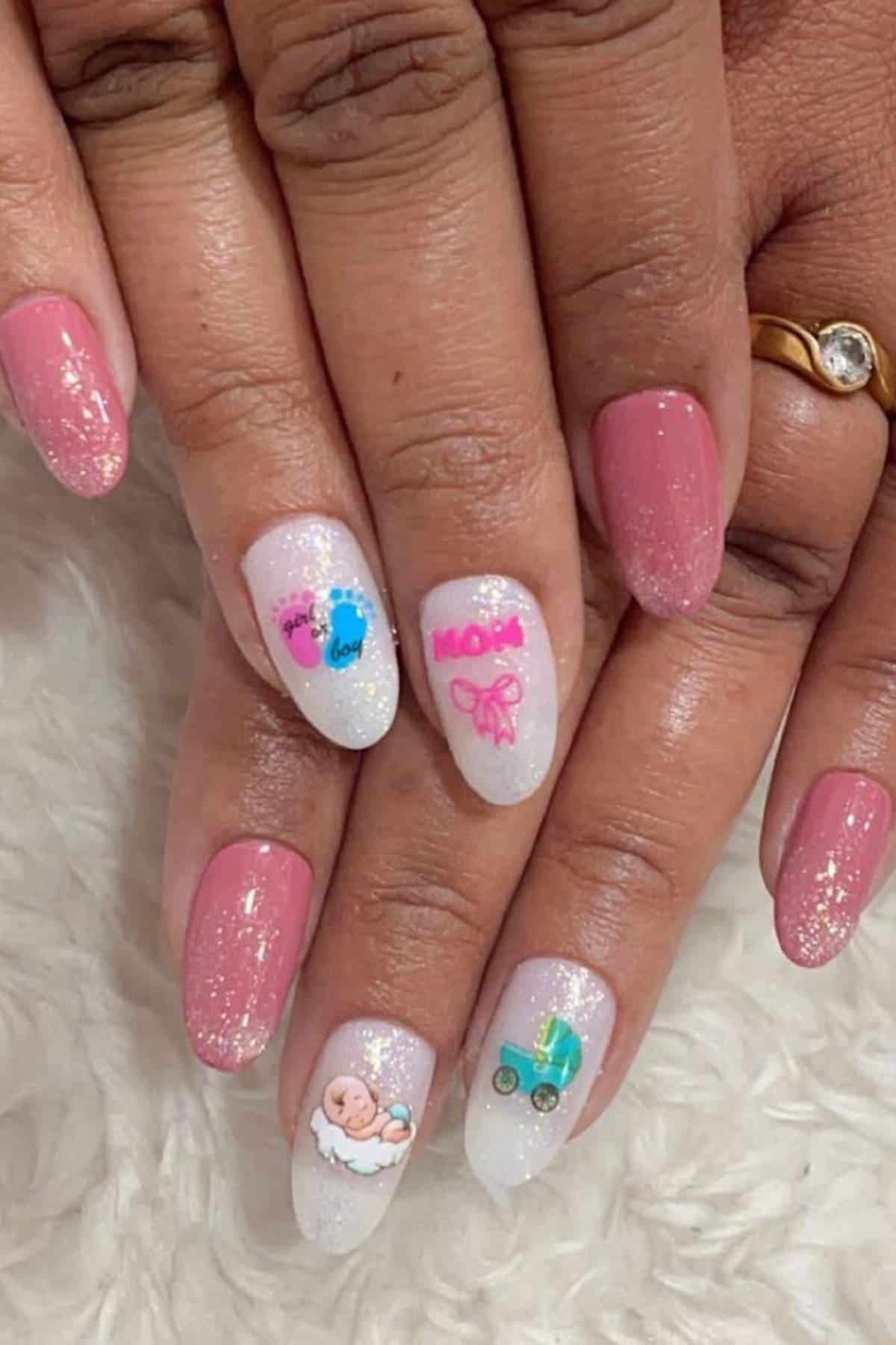 A hand with pink and white glitter ombré nails featuring baby-themed stickers, including a stroller, a bow, footprints, and a baby.