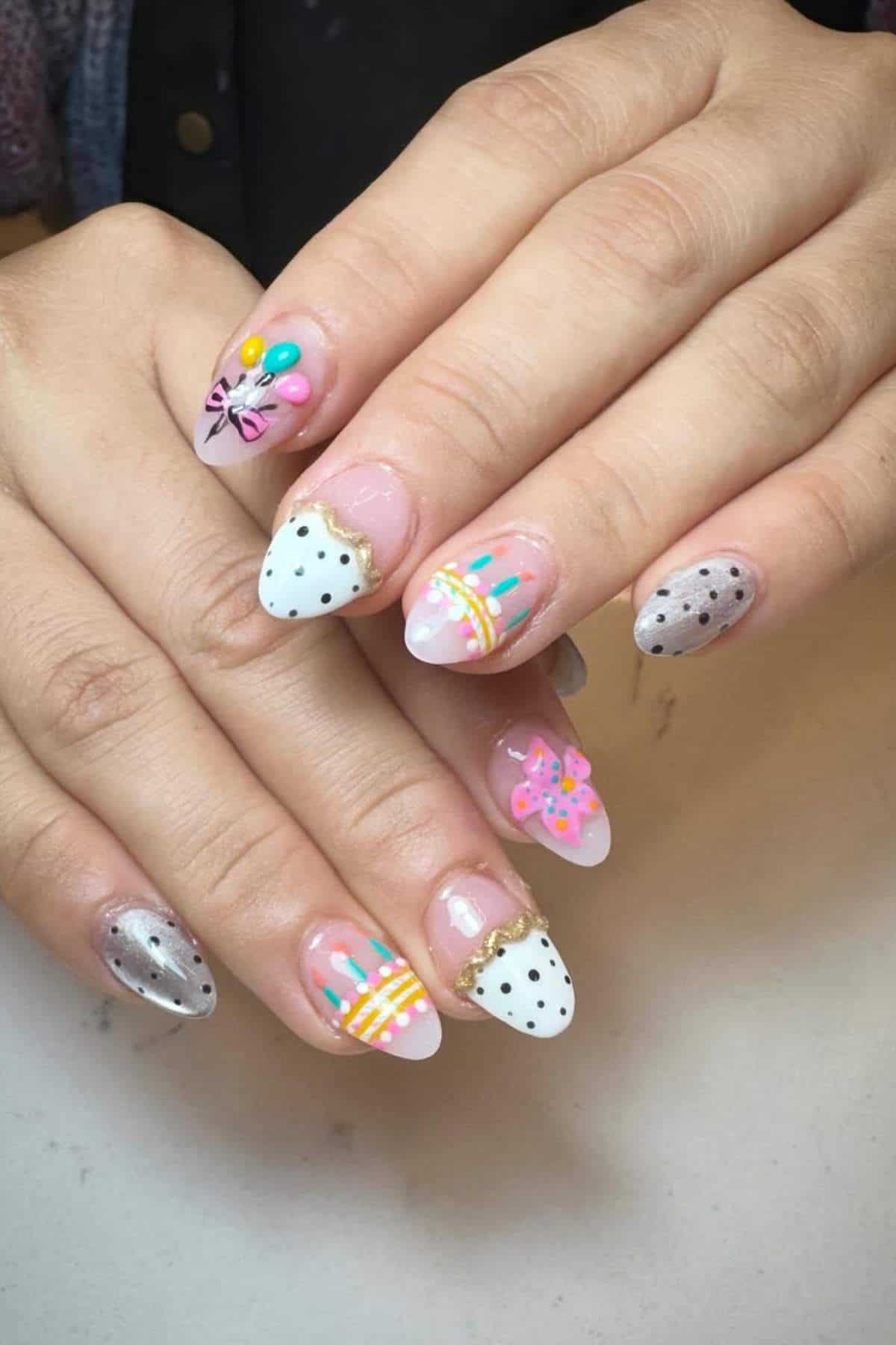 Hands with manicured nails featuring various designs, including polka dots, stripes, flowers, butterflies, and metallic silver accents on a light background.