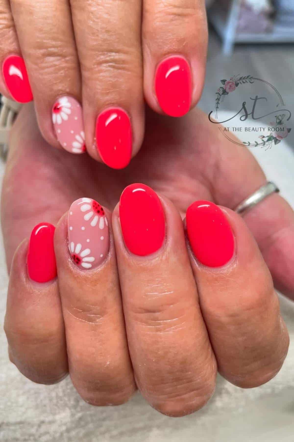 Close-up of hands with bright pink oval nails; two accent nails feature white and red daisy flower designs on a nude base.