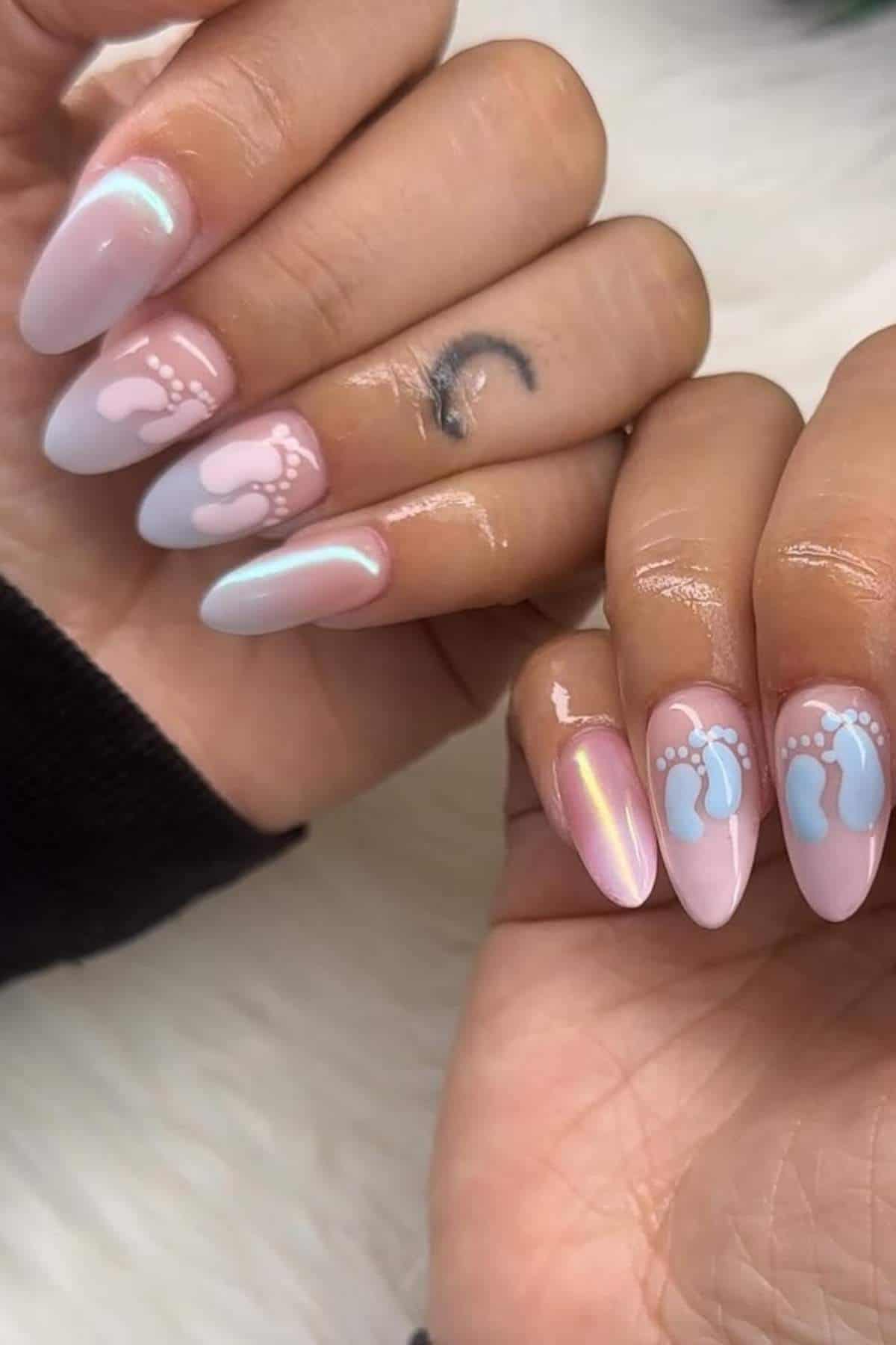 Hands with long, almond-shaped nails painted in pearly pastel colors, featuring small blue and white baby foot designs on some nails.