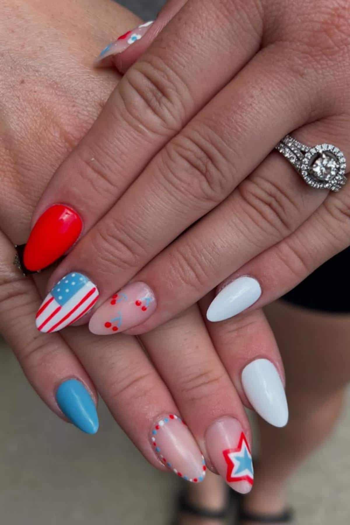 Hands with manicured nails featuring red, white, and blue designs, including stars, stripes, and polka dots; a diamond ring is worn on one finger.