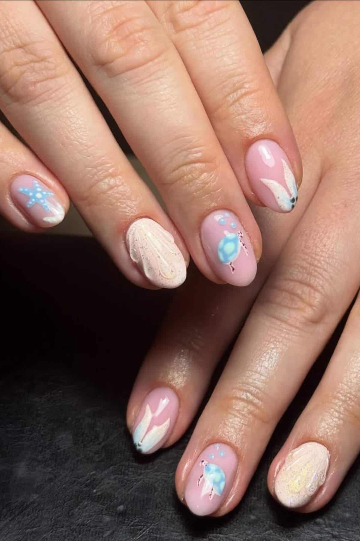 Close-up of hands with short, almond-shaped nails featuring pink base polish and pastel abstract designs with blue and white accents.